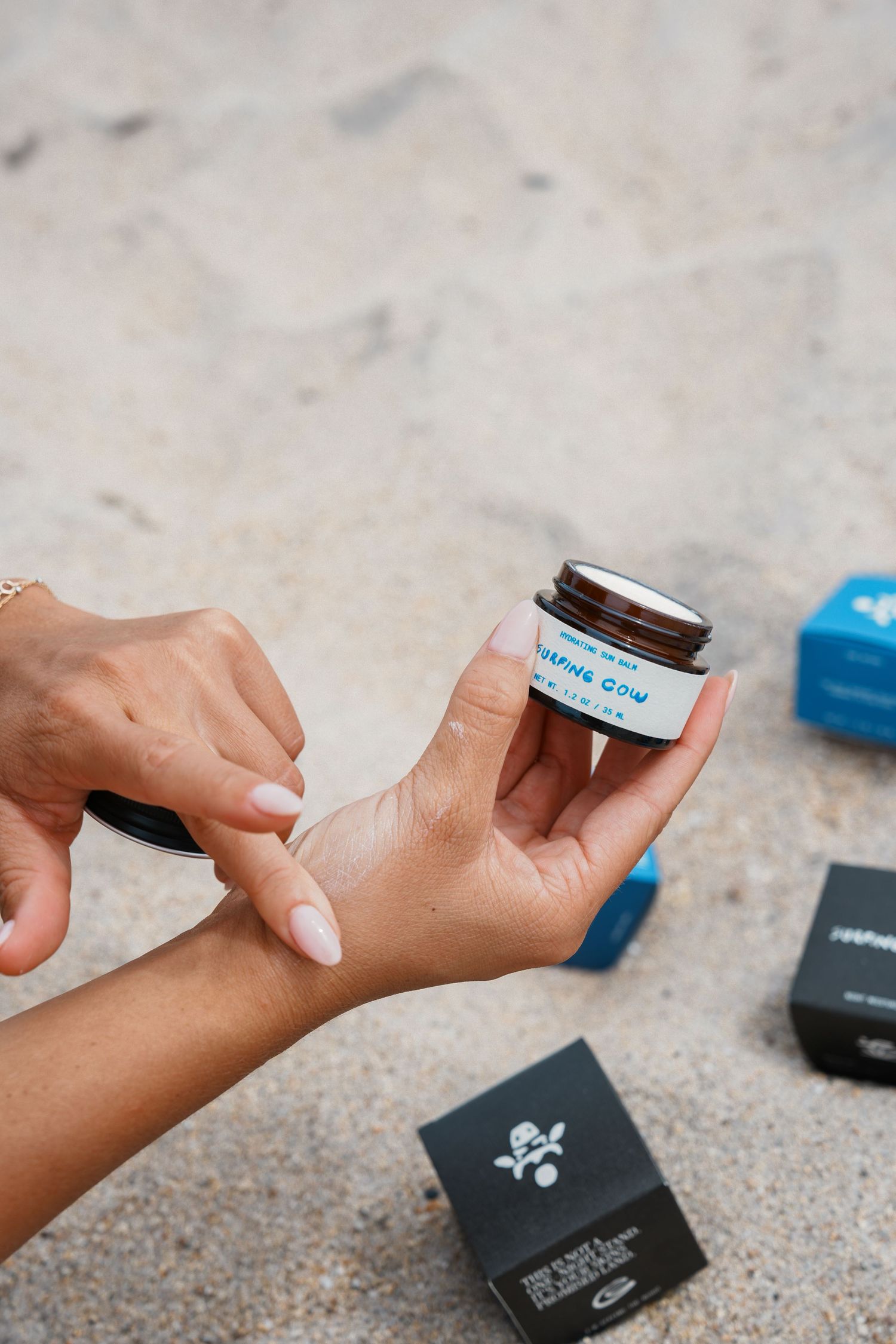 Close-up shots of hands applying sunscreen or skincare cream from a black jar against a textured surface.