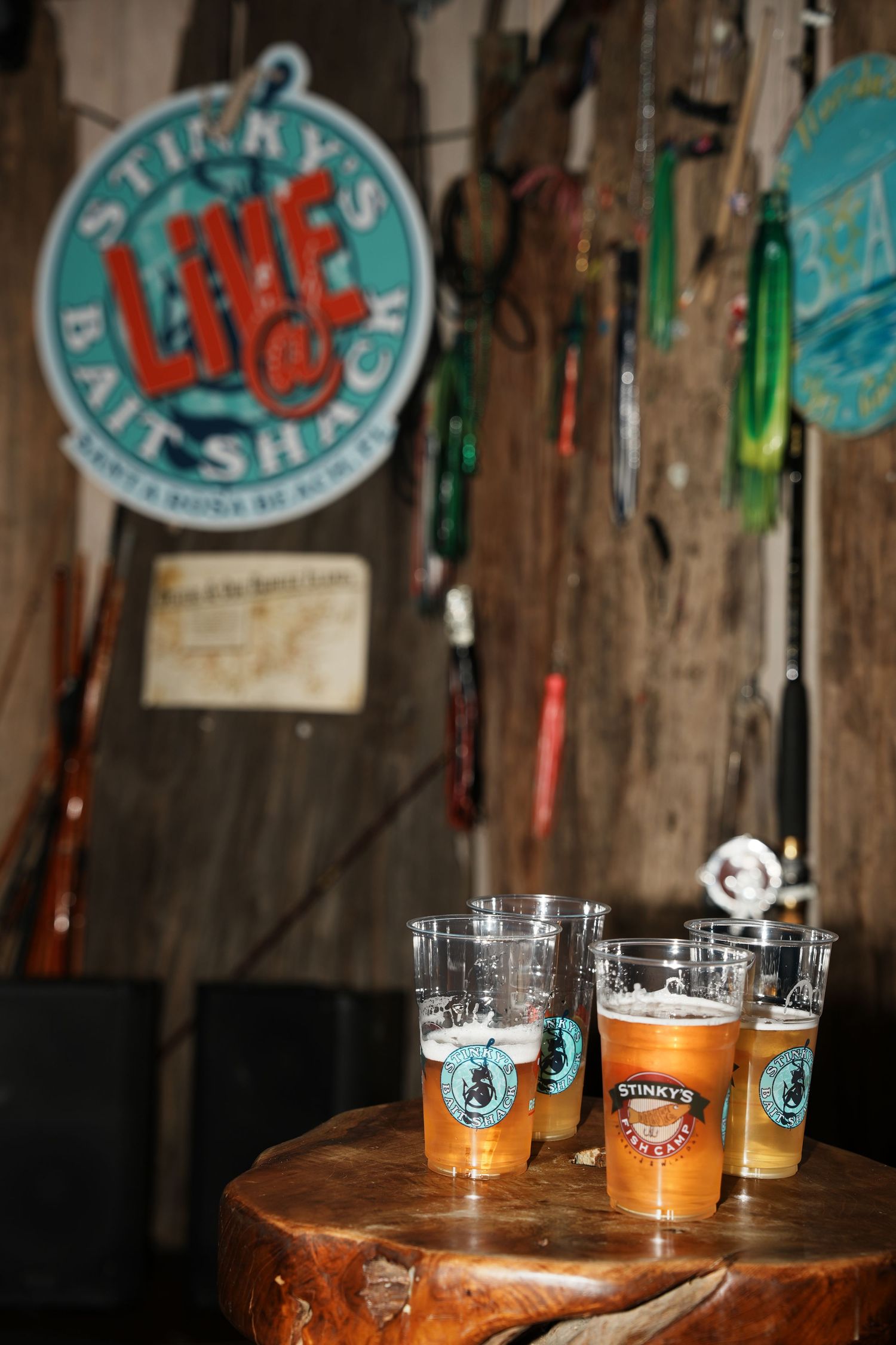 Several craft beer glasses filled with golden ale sit on a rustic wooden table beneath a vintage Live bar sign.