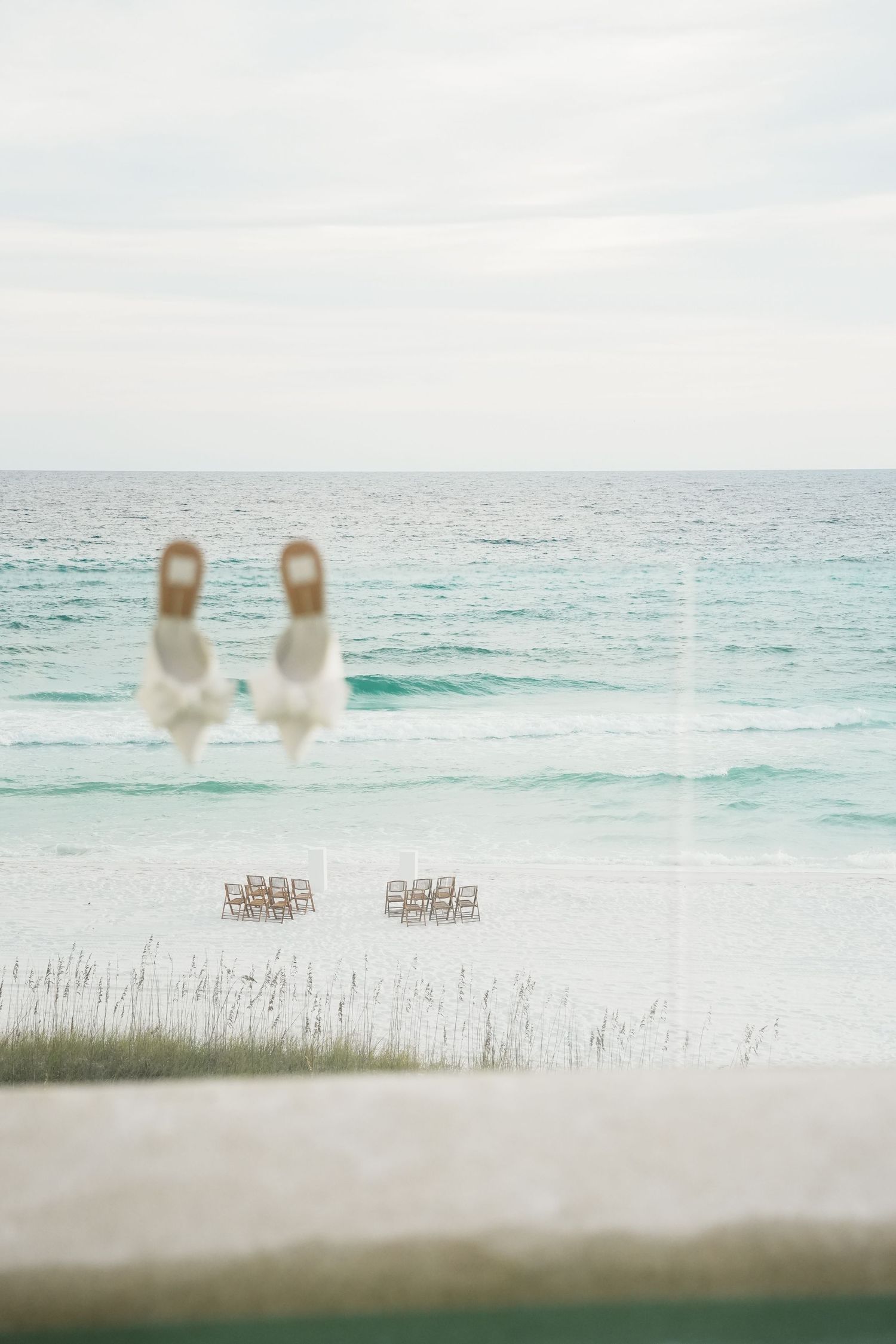 Empty white chairs set up for a beach wedding ceremony with turquoise ocean waves in the background.