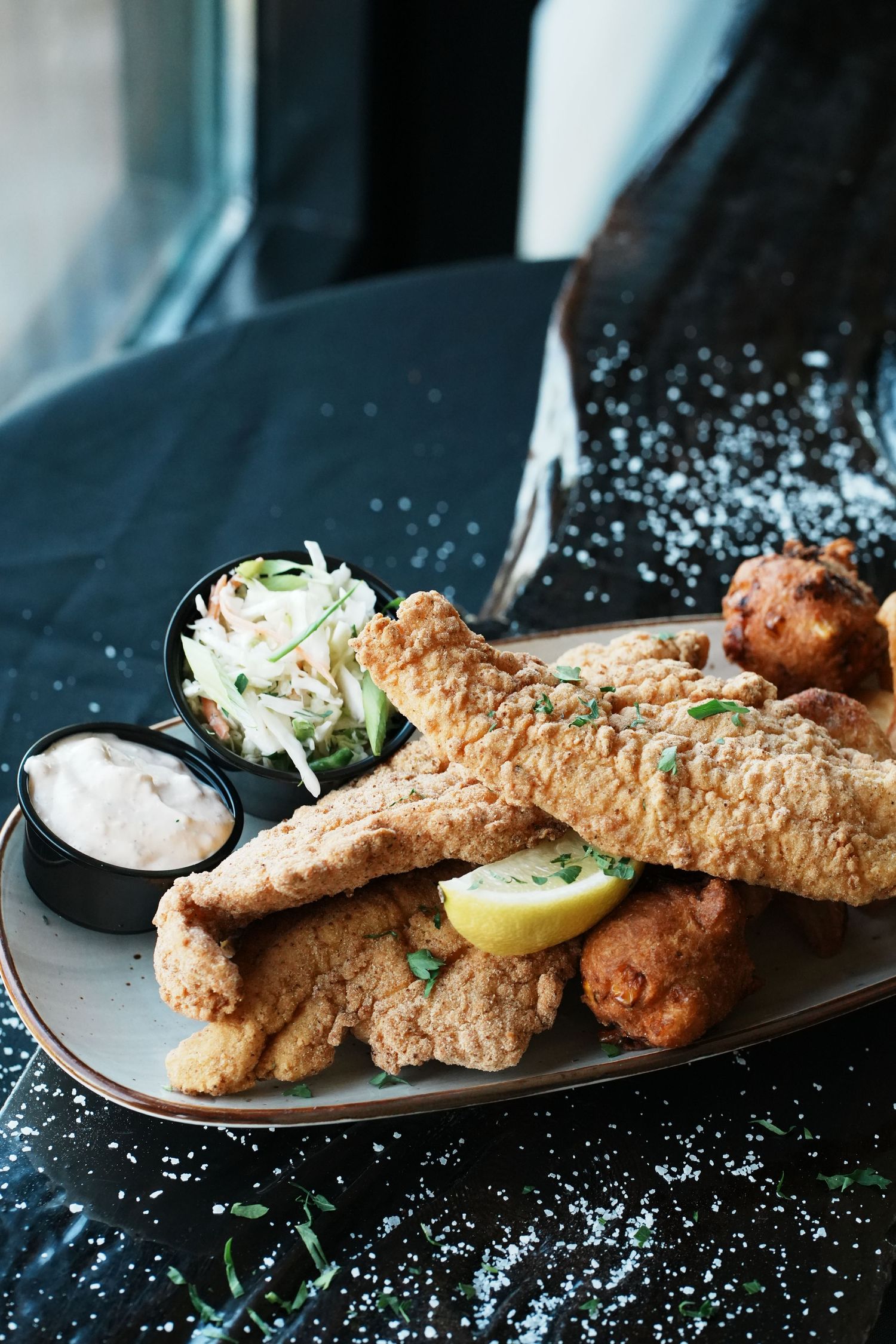 Crispy fried fish fillets served with coleslaw and lemon on a black plate.