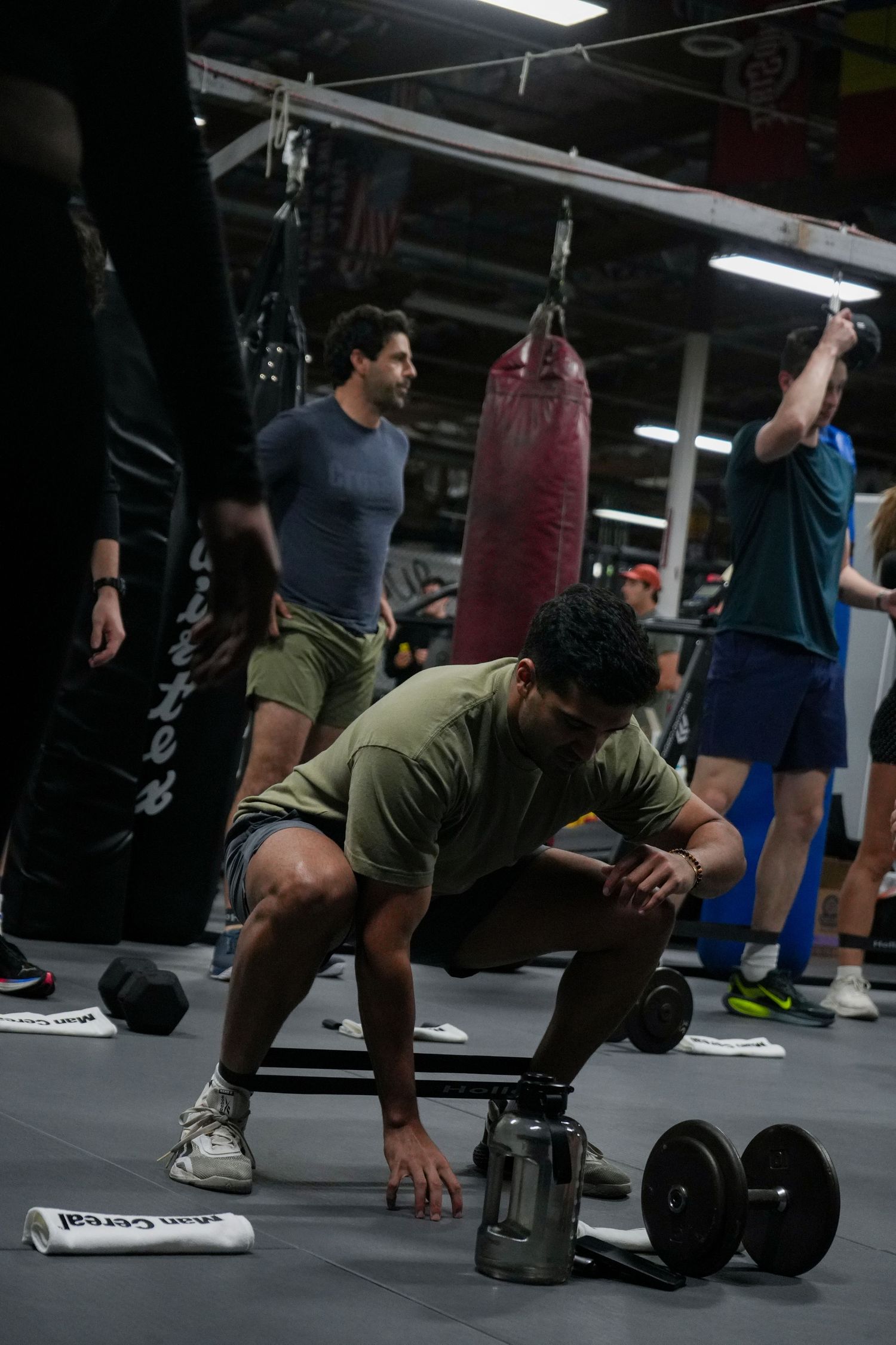 Person performing a dumbbell exercise on the floor in a gym with punching bags in the background.