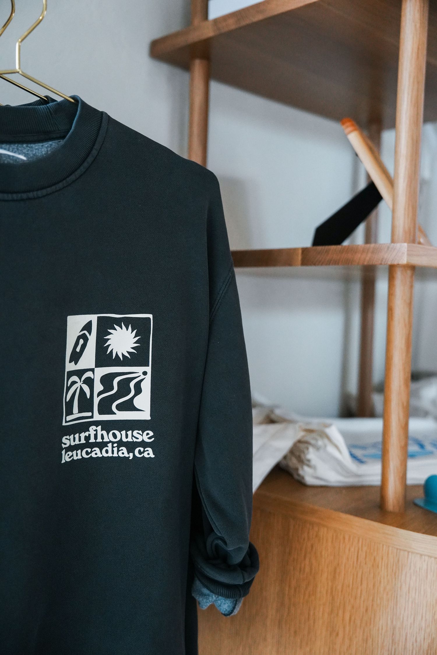 A black long-sleeve shirt with a surf house logo featuring palm trees and waves from Leucadia, California.