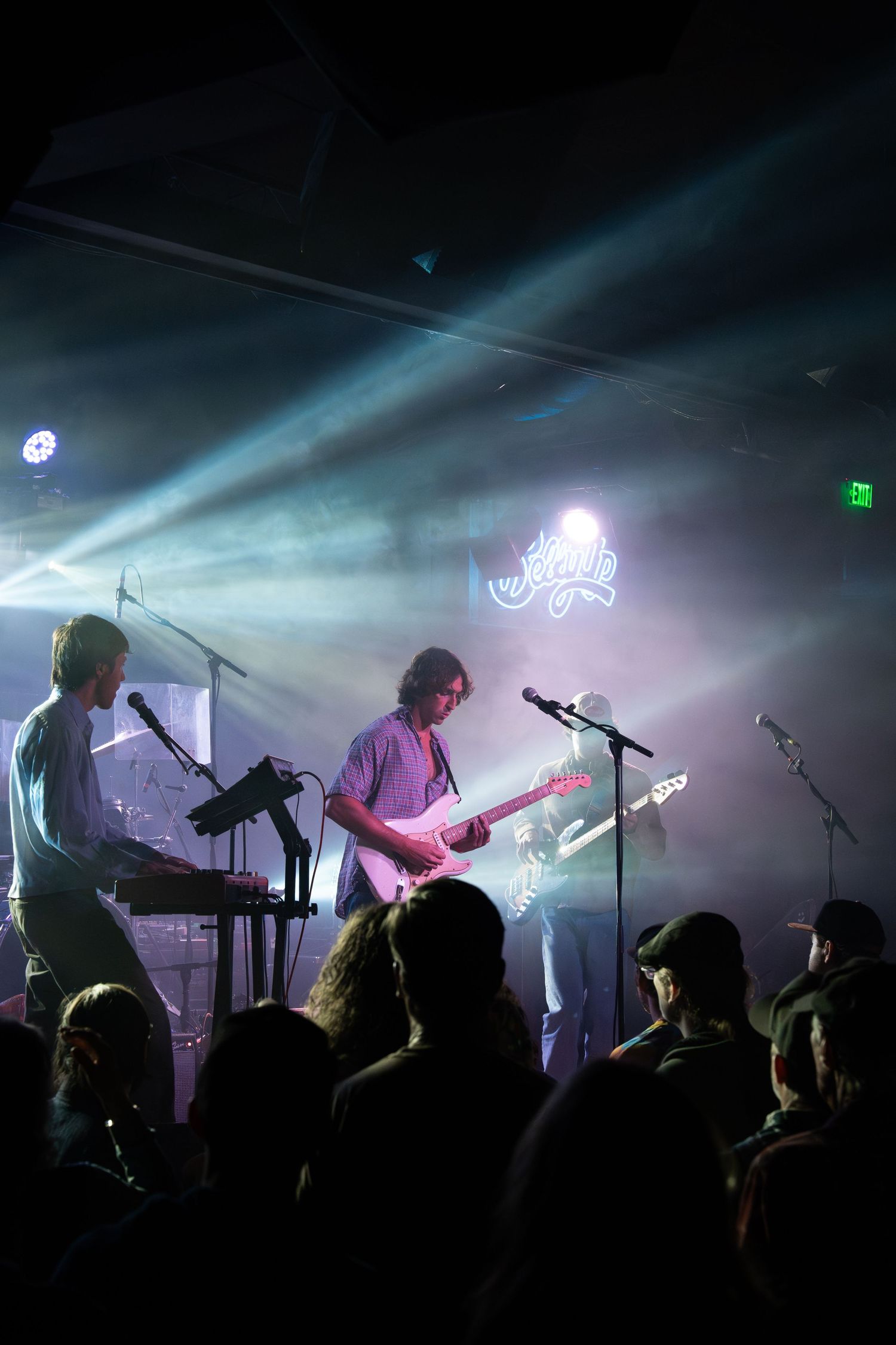 Silhouetted musicians perform on a dark stage with atmospheric fog and dramatic lighting during a live concert performance.