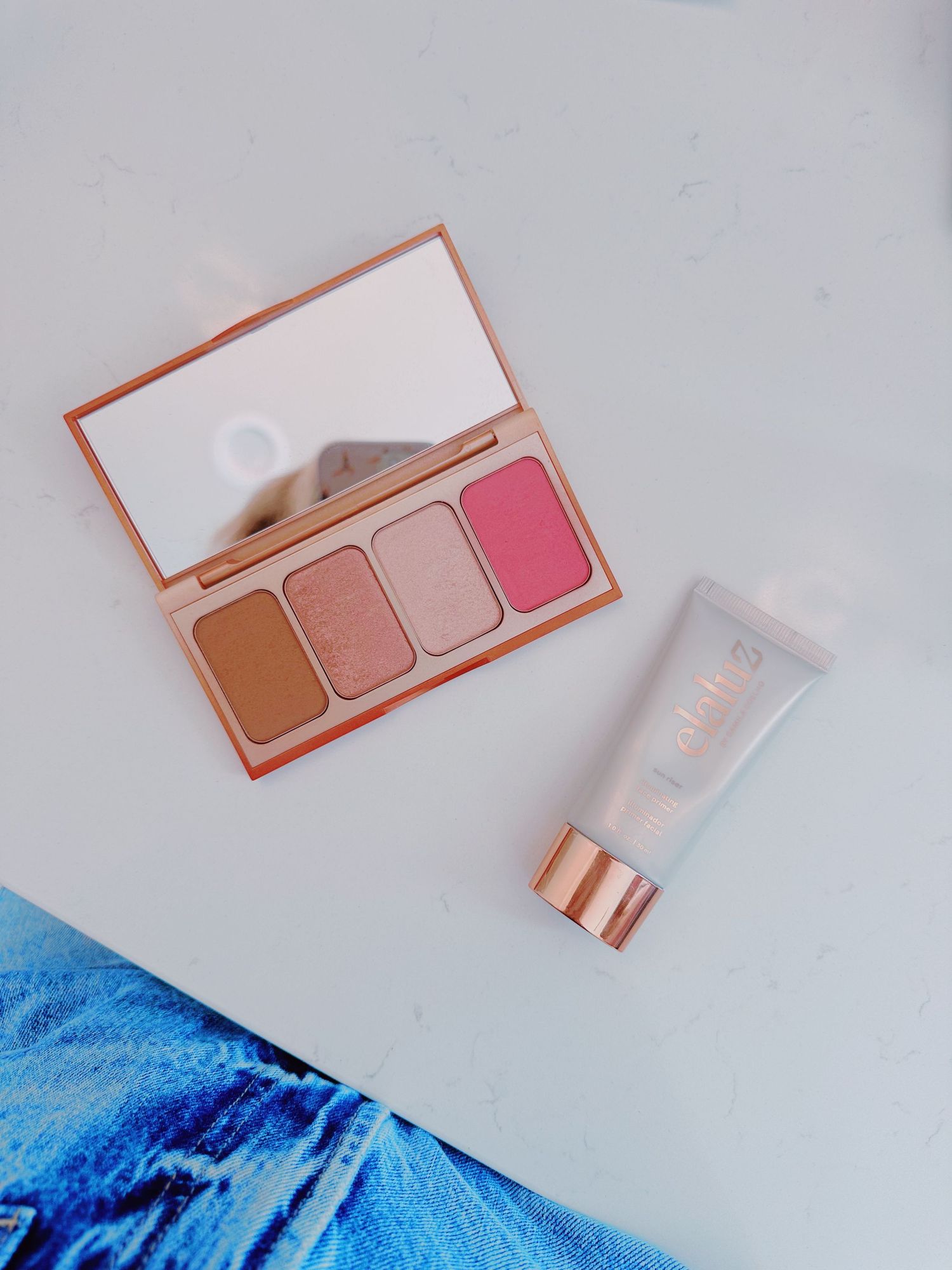 Makeup palette with neutral tones and pink tube against blue background.