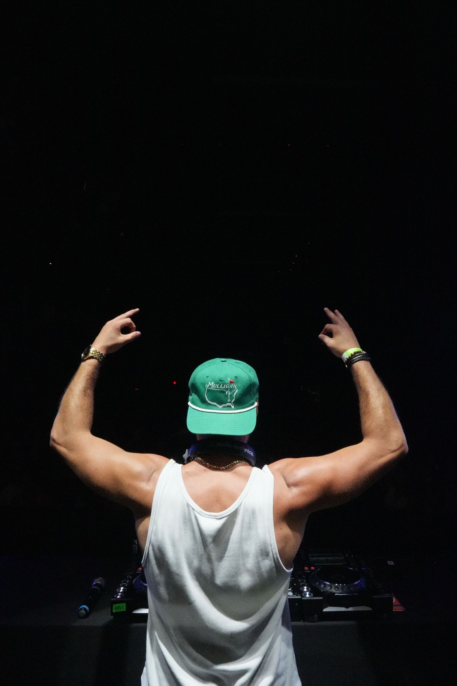 Person in white tank top and green cap showing muscular back poses against dark background.