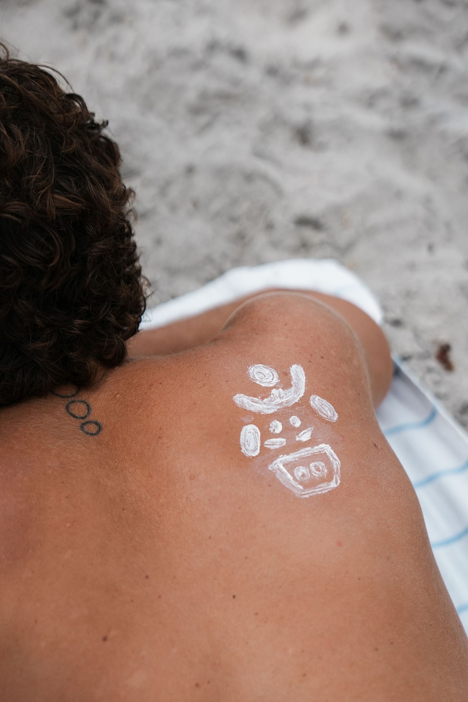 White sunscreen drawing of a happy face on a person's back at the beach.