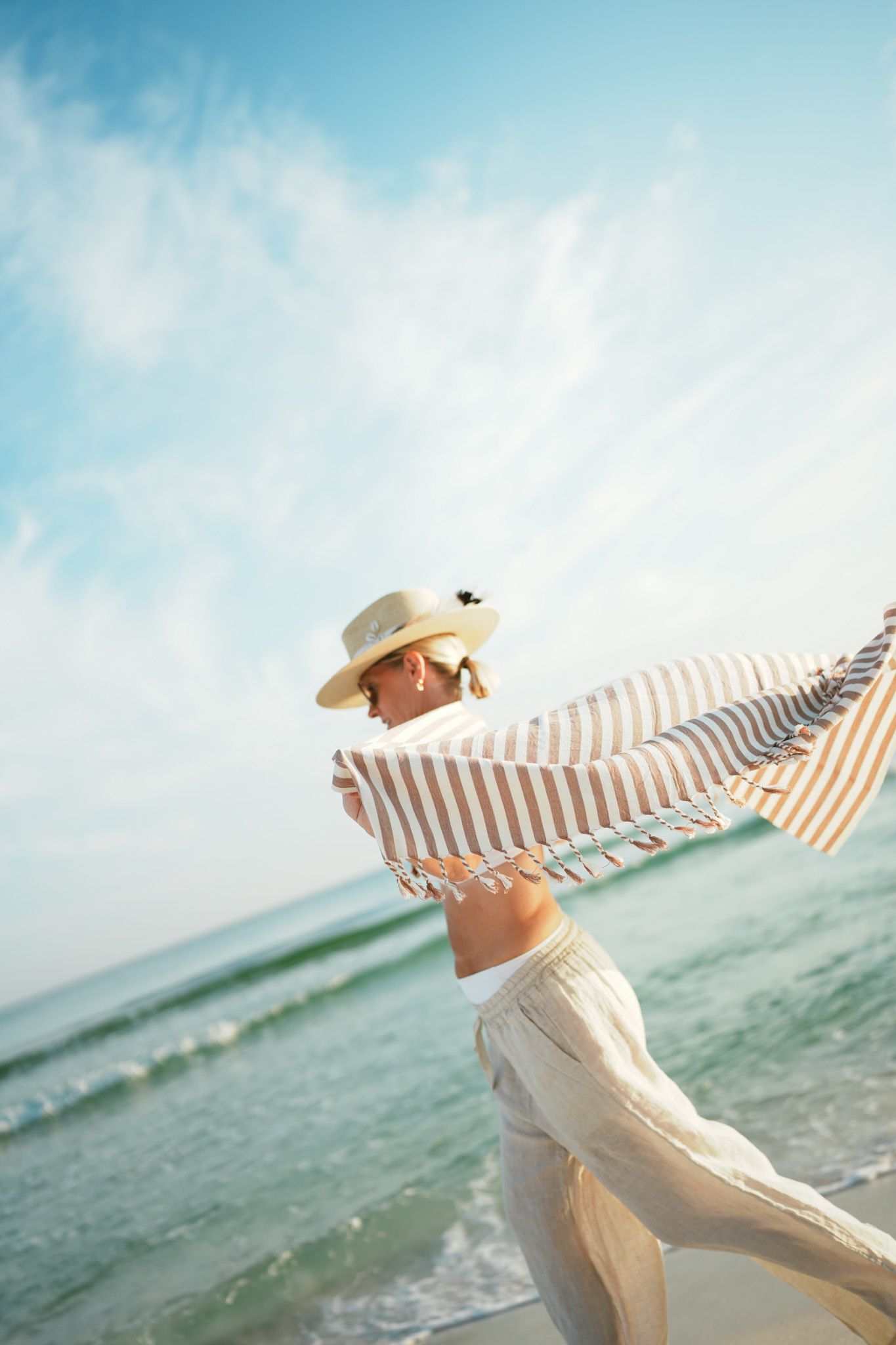 Woman in white dress and sun hat runs joyfully along beach on bright sunny day by turquoise ocean waters.