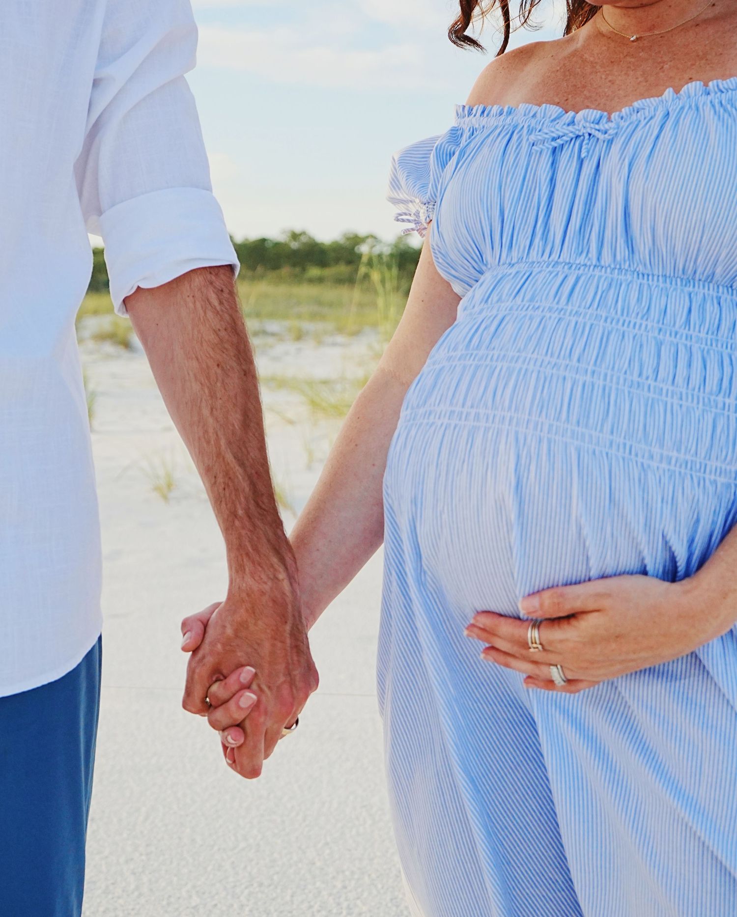 Couple holding hands on a beach wearing coordinating light blue and white summer outfits.