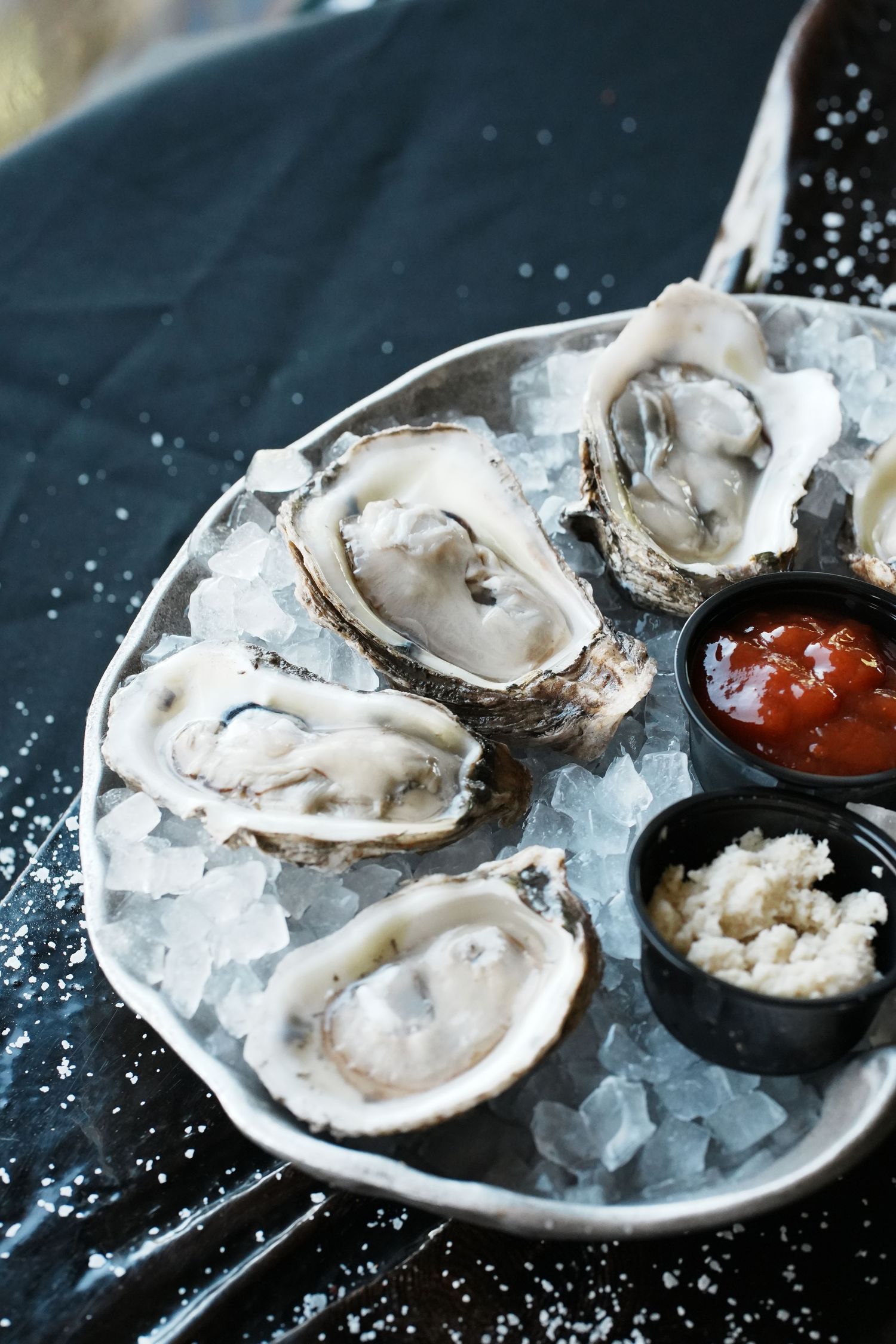 Fresh raw oysters on ice served with cocktail sauce on a dark plate in a seafood restaurant setting.