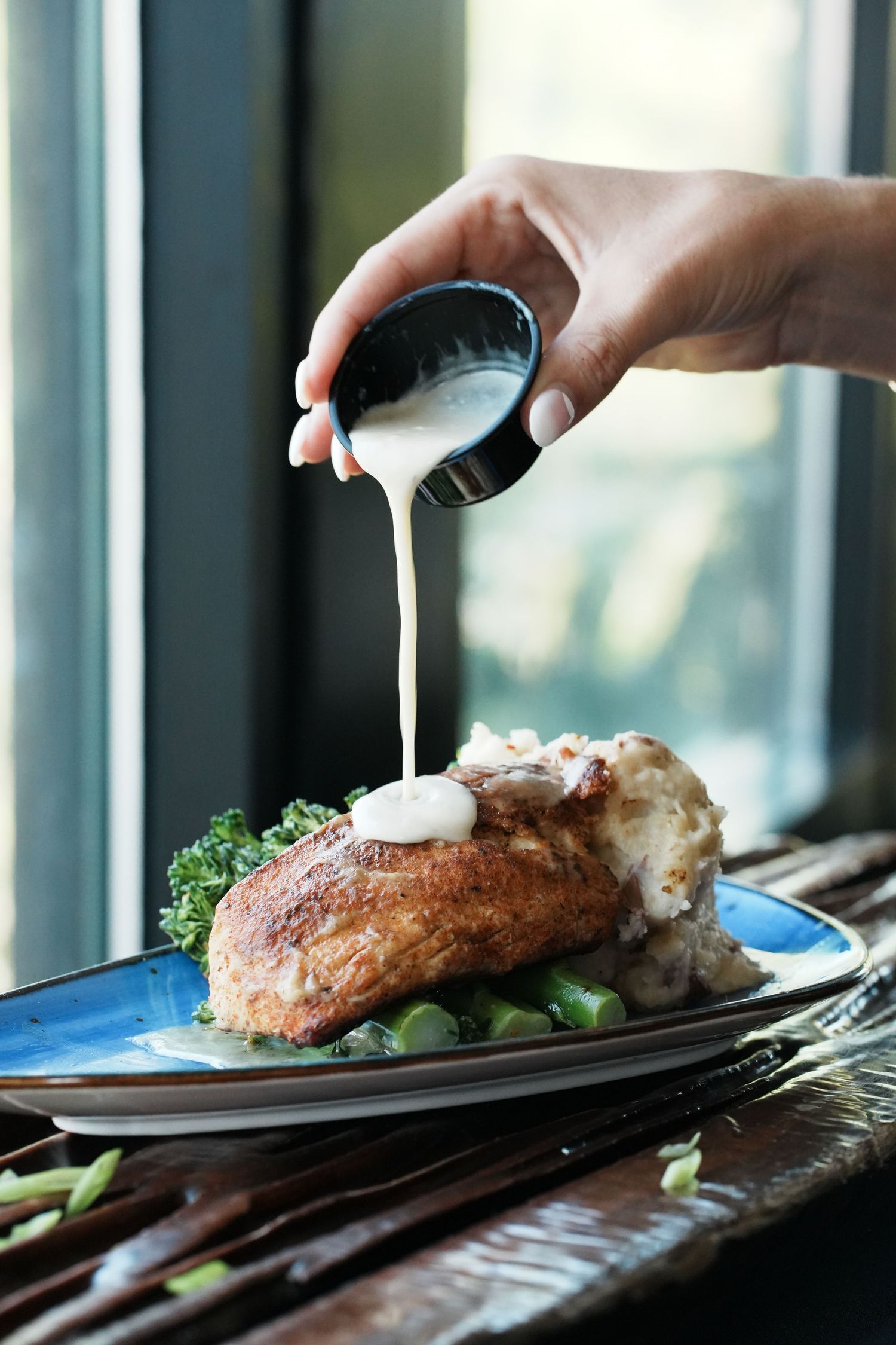 Hand cutting into a perfectly cooked fish fillet with vegetables on a dark plate.