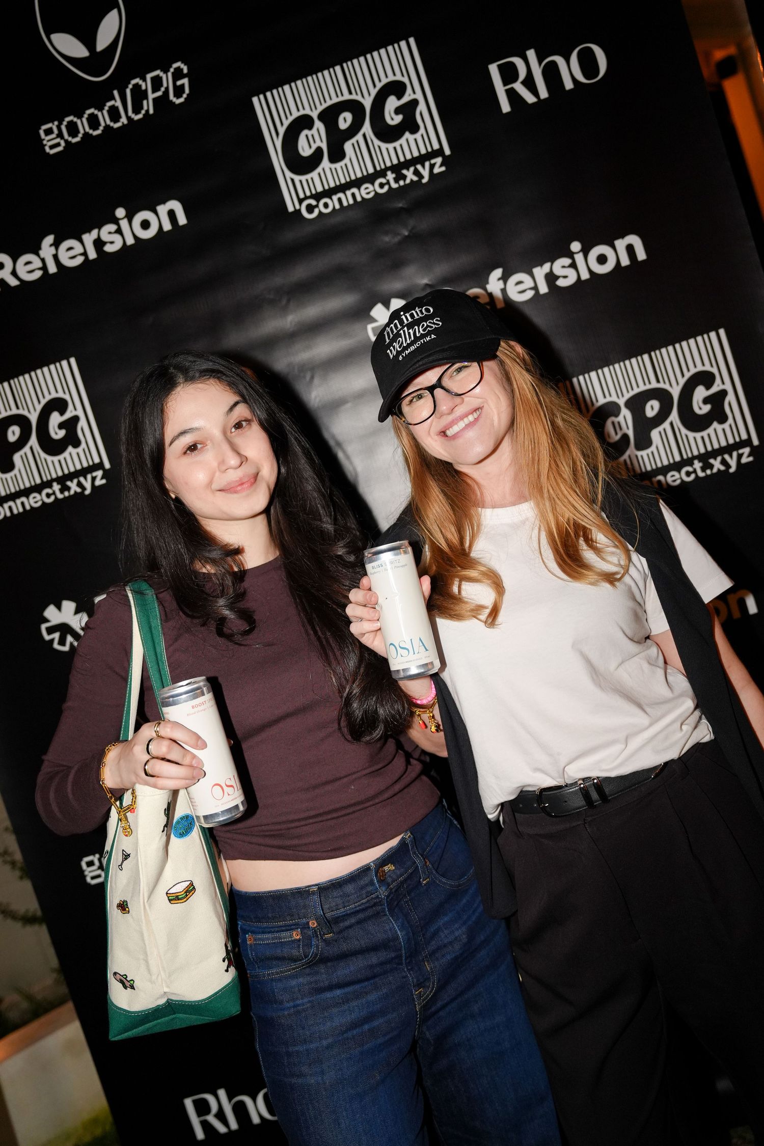 Group of attendees holding beverages at a nighttime event with promotional banners in the background.