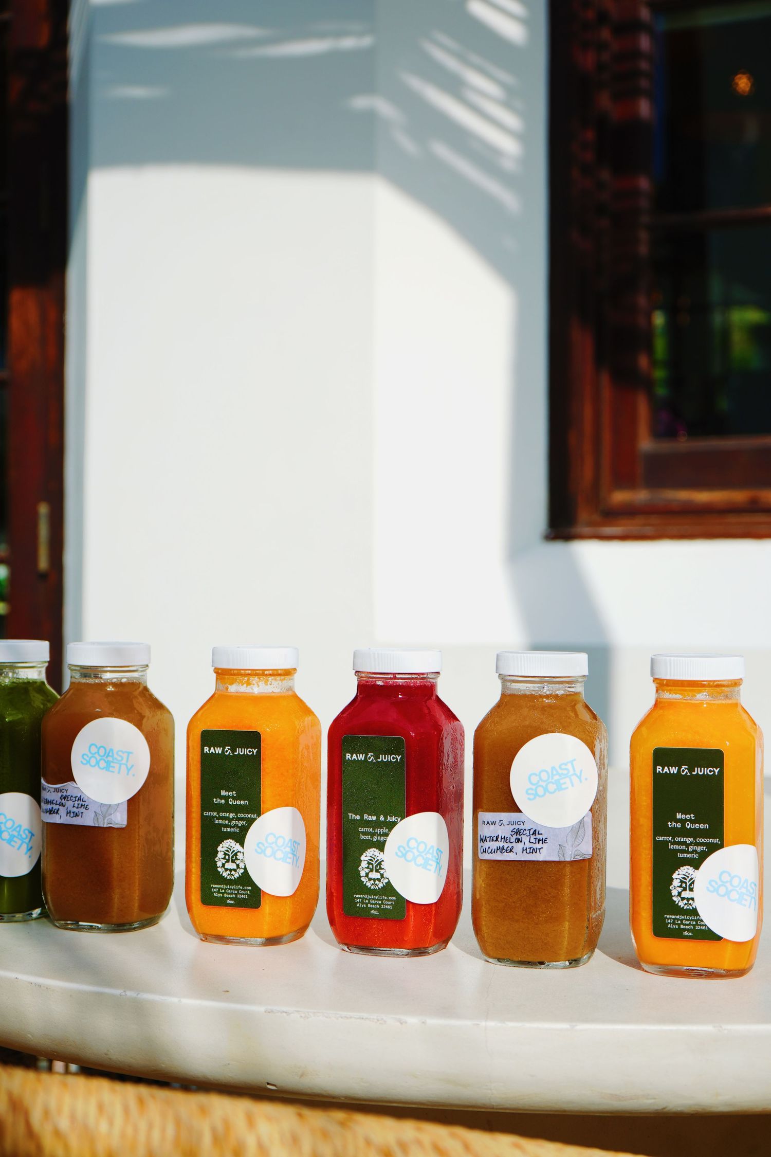 Colorful glass bottles of fresh pressed juices lined up on white surface showing different flavors from orange to red.