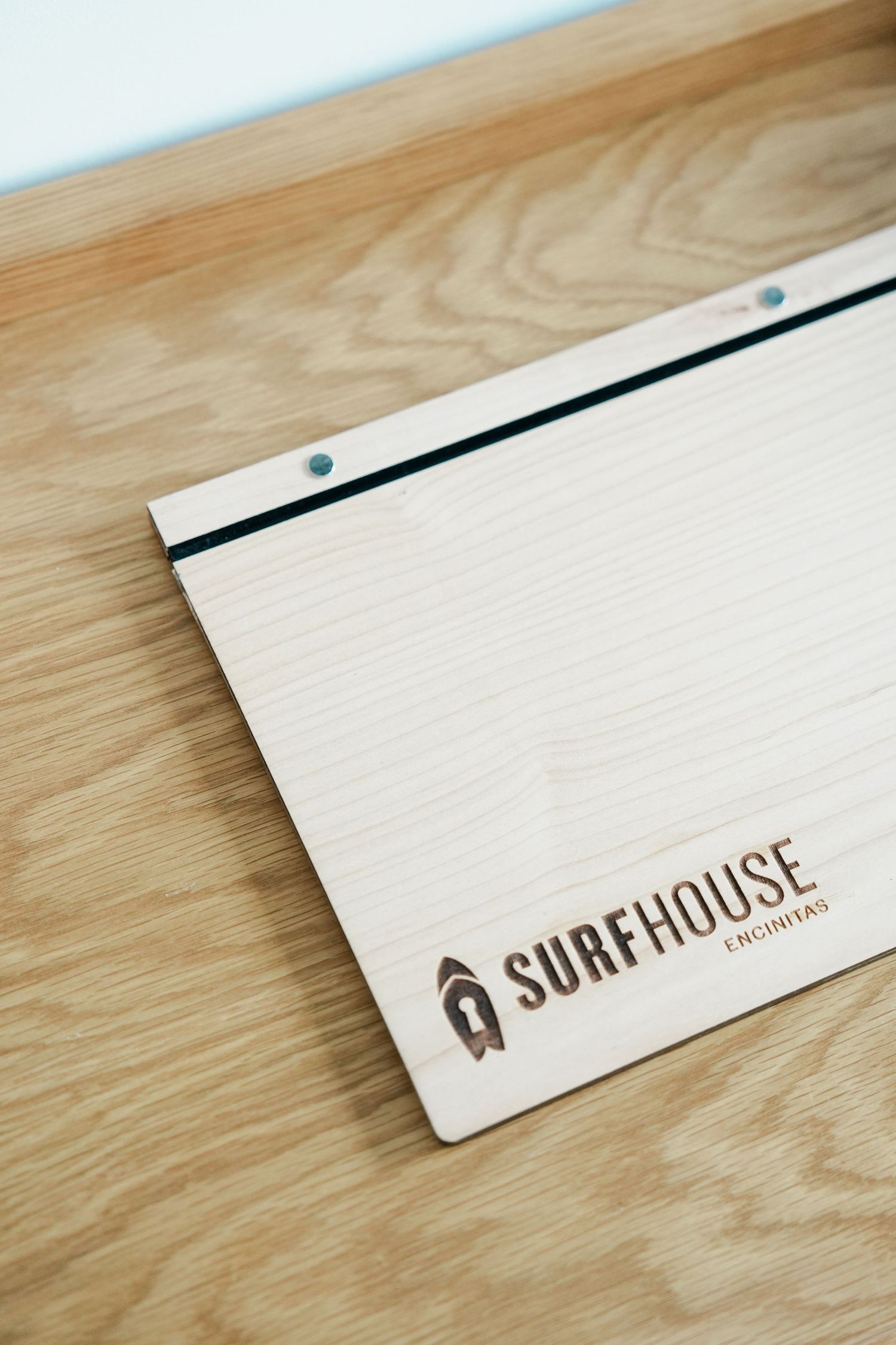 Wooden surface with minimalist surfhouse branding text in brown showing progressive reveal of logo design.