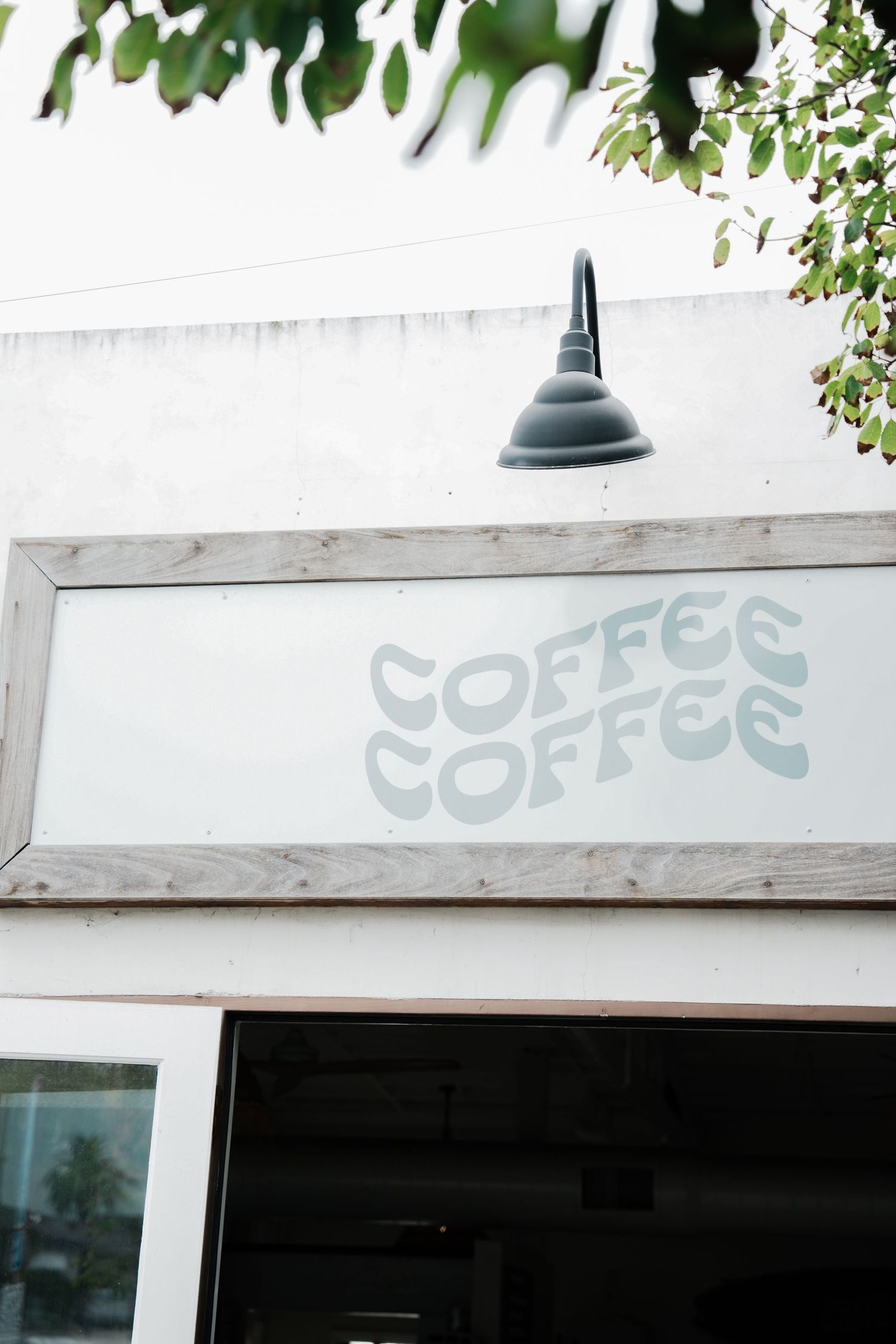 A coffee shop exterior sign with 'COFFEE COFFEE' text and a black gooseneck lamp mounted above.