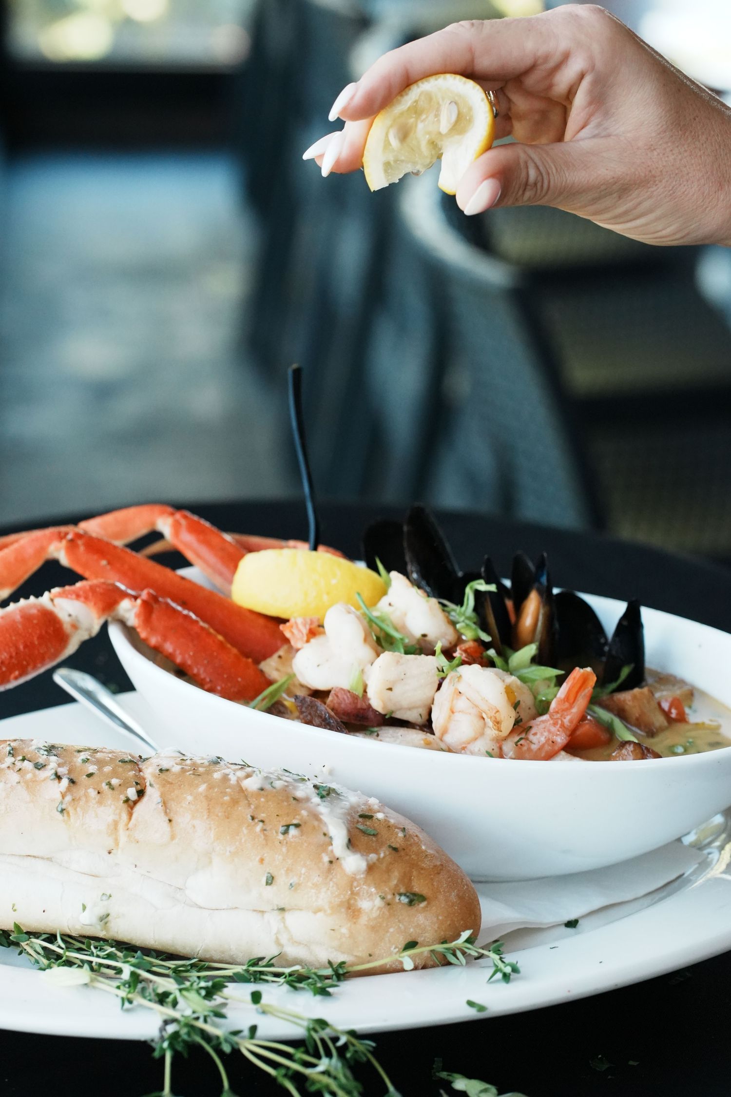 Fresh seafood dish being garnished with lemon on a white plate with fresh herbs.