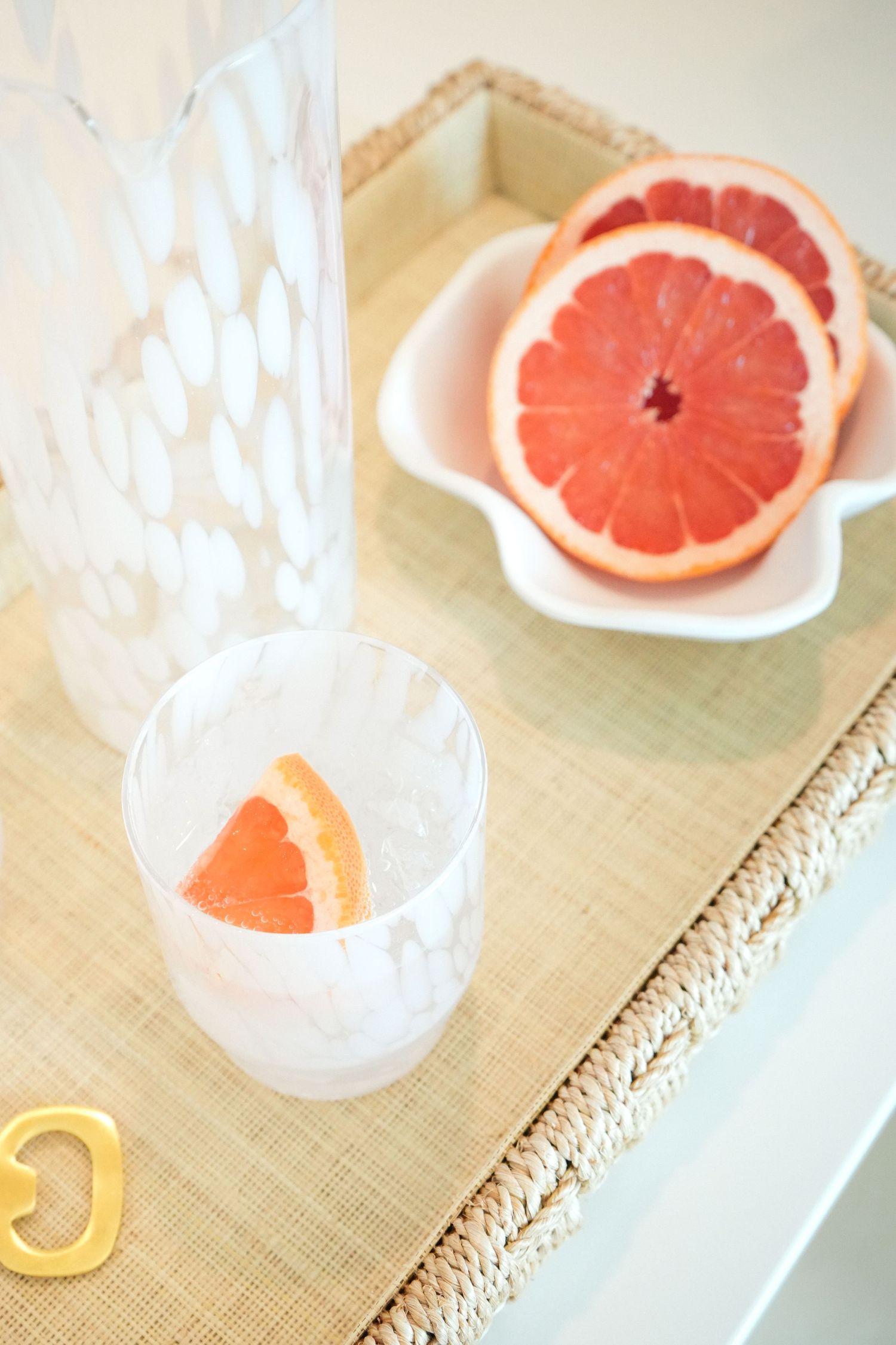 Fresh grapefruit slices arranged on a pink plate with a glass of citrus water on a beige table mat.
