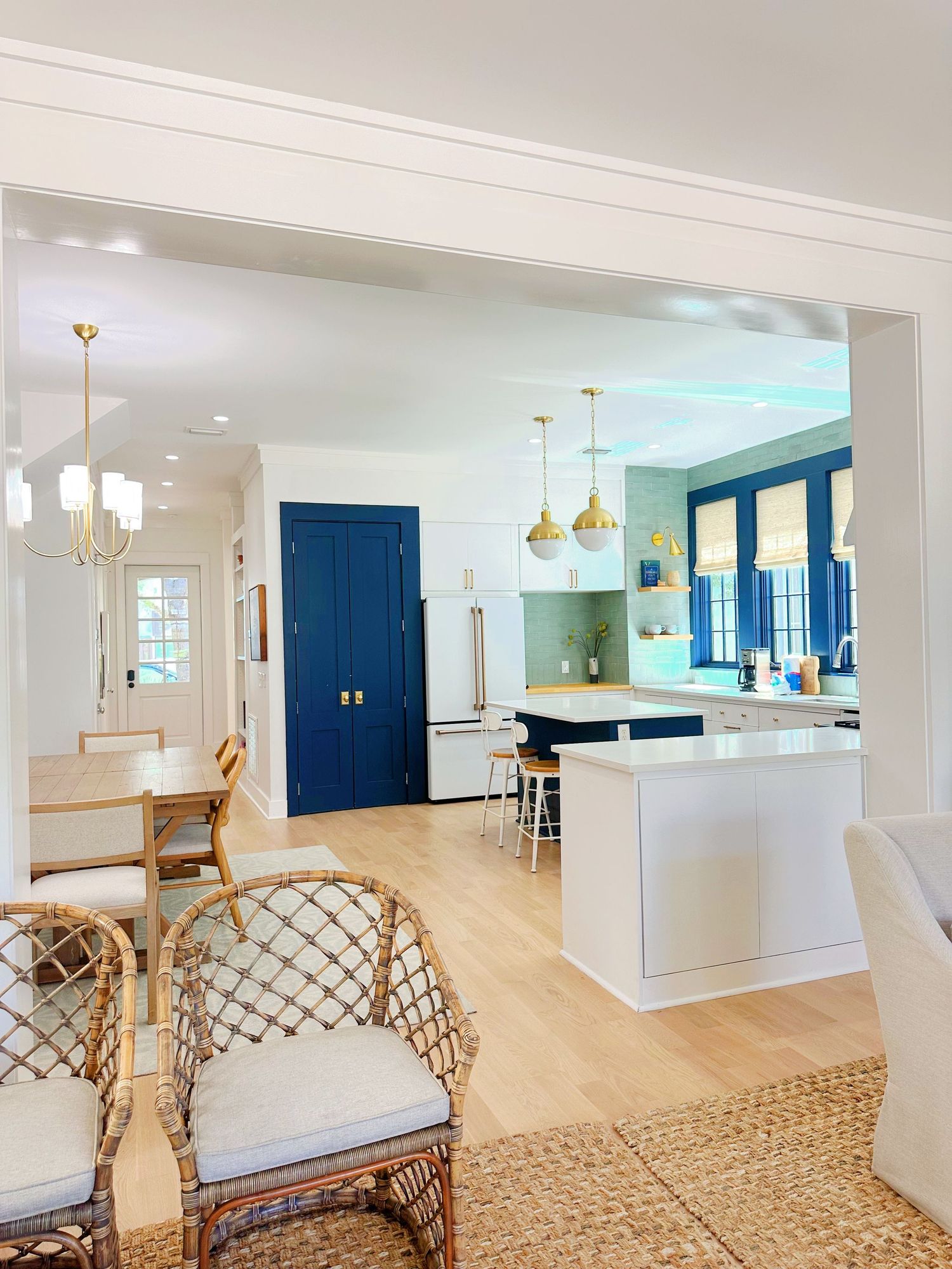 Modern coastal kitchen with navy blue accents, rattan chairs, and gold pendant lights.