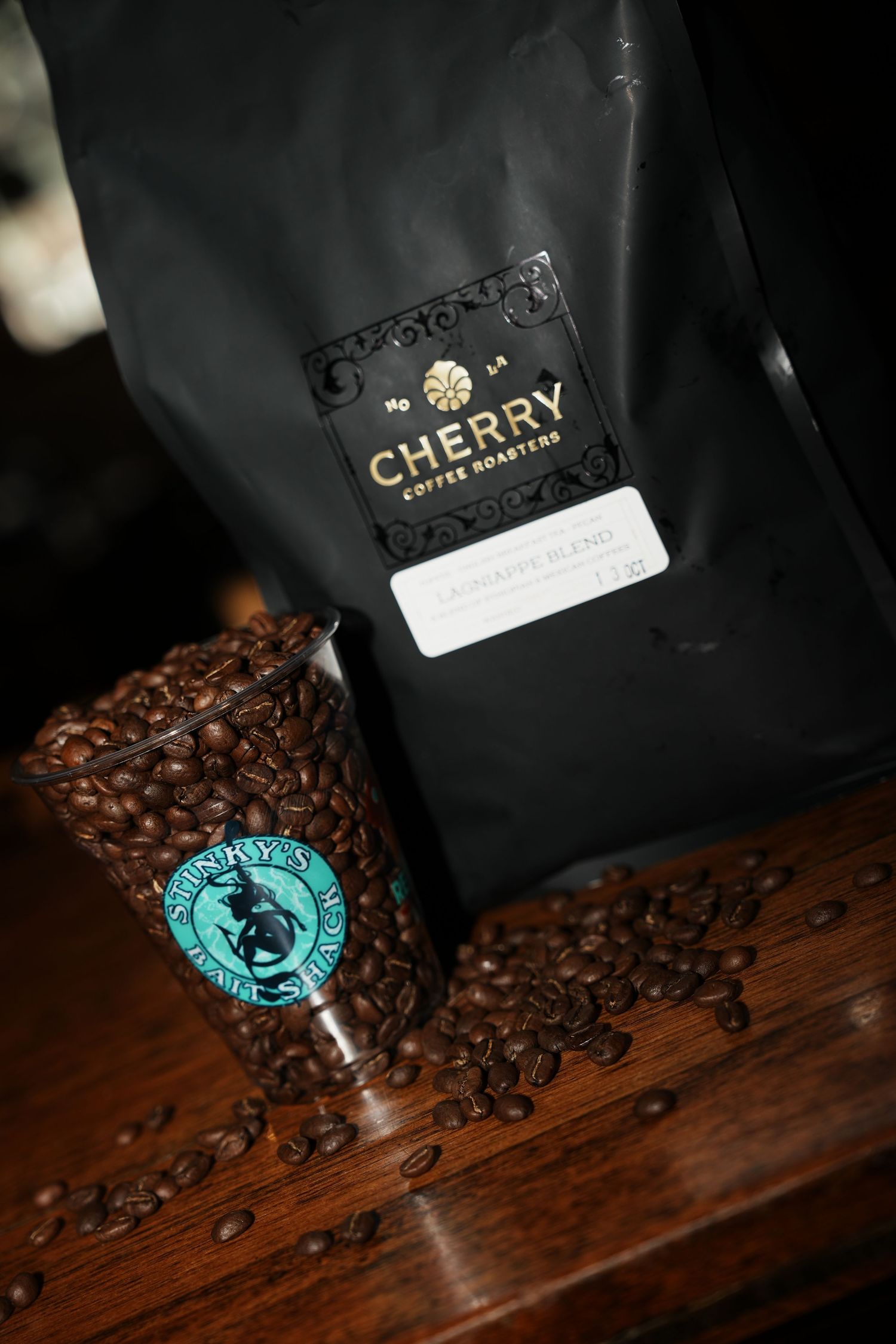 Black coffee bags with brand logos and scattered coffee beans on a dark wooden surface.