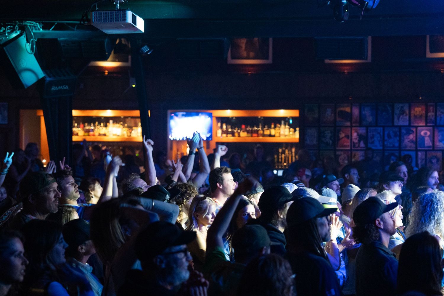 Crowded nightclub interior with blue lighting and people dancing on a dark dance floor.