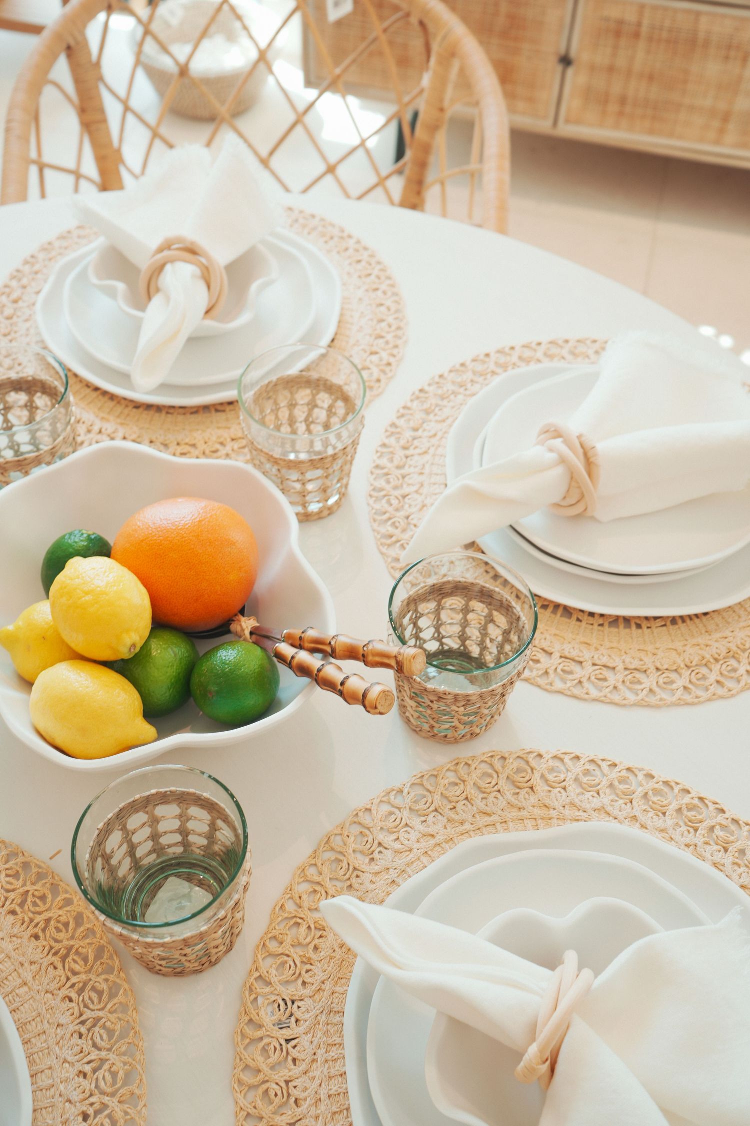 Elegant table setting with lace tablecloth, white plates, crystal glasses and fresh citrus fruits in white bowl.