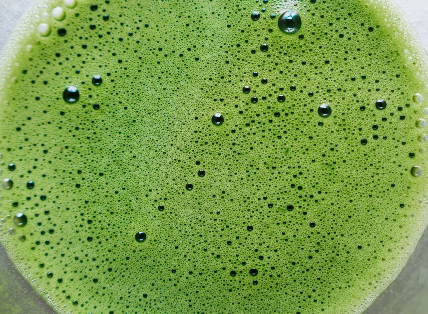 Bright green matcha tea with tiny bubbles and foam creates a frothy texture in a white cup.