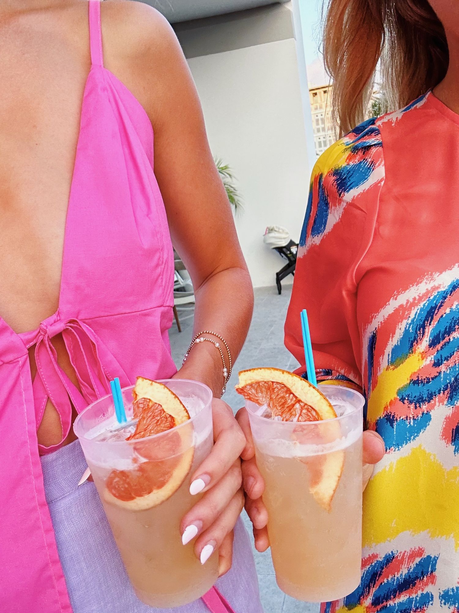 Two fruity cocktails garnished with citrus slices held by people in colorful summer outfits.