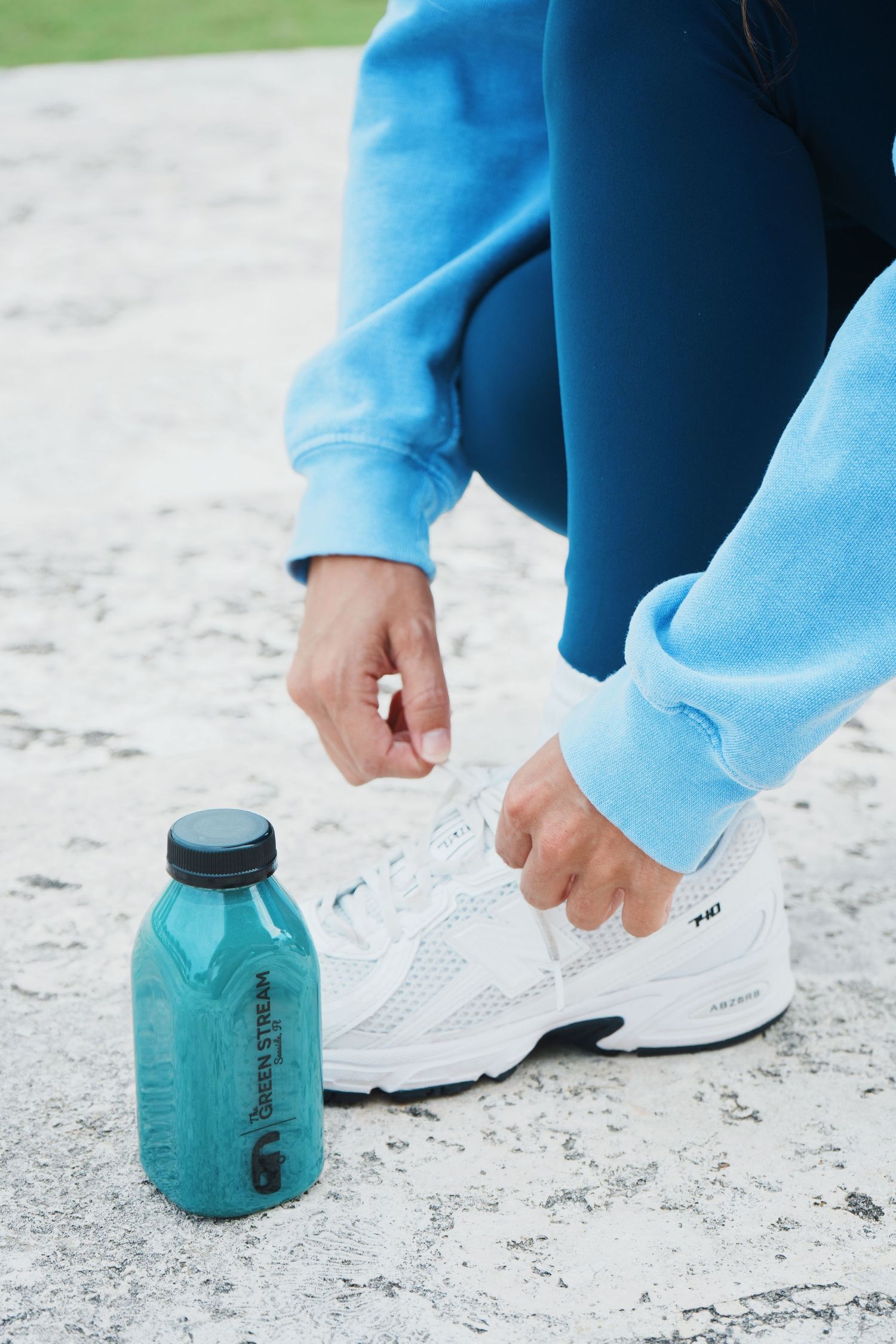Close-up of turquoise water bottle and white athletic shoes on concrete during workout session.