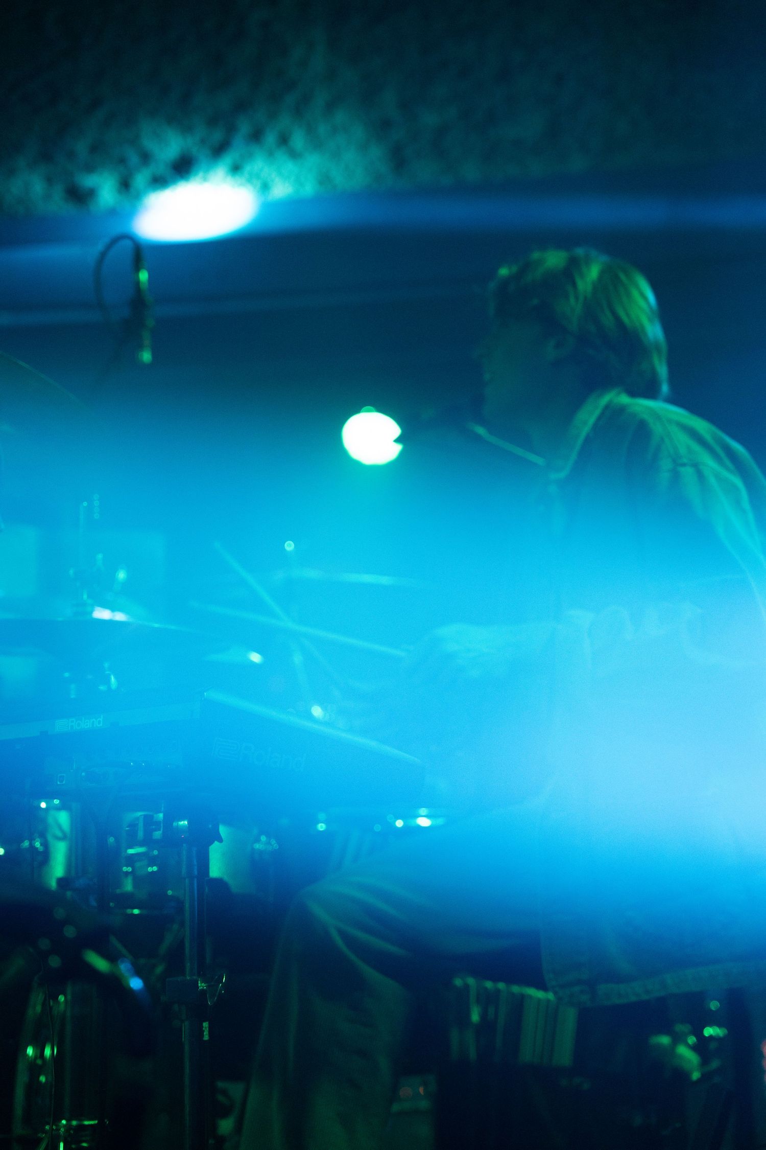 Blue and green spotlights illuminate a dark nightclub atmosphere with hazy smoke effects creating a moody ambiance.