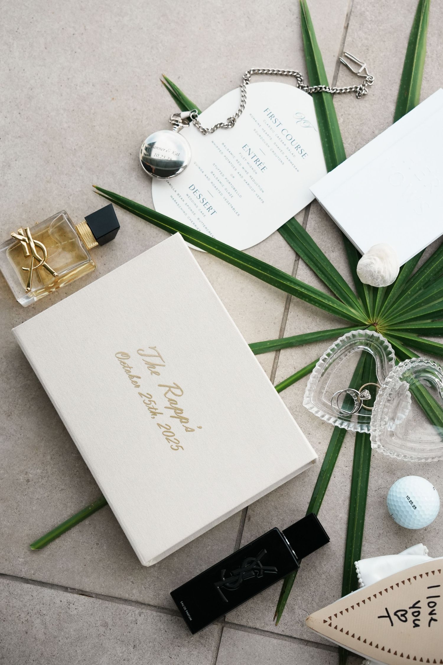 Minimalist wedding stationery set with palm leaves, white cards, and gold accents on a gray surface.