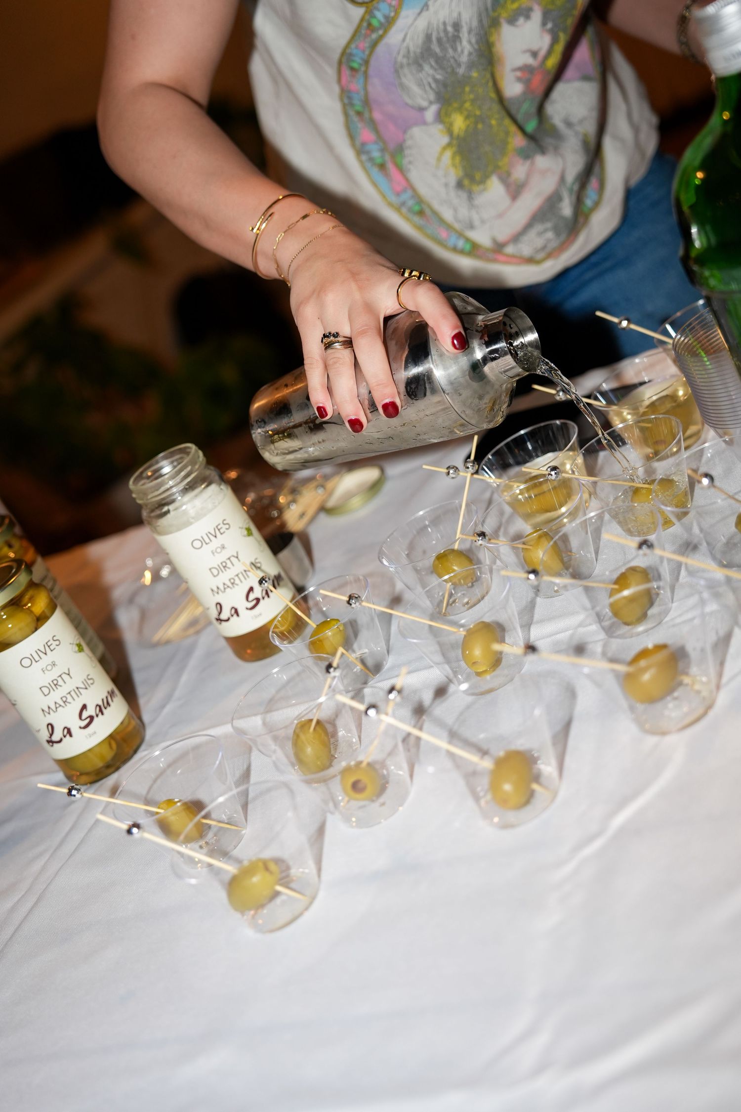 Hands arranging small glasses and bottles on a white tablecloth at an event.