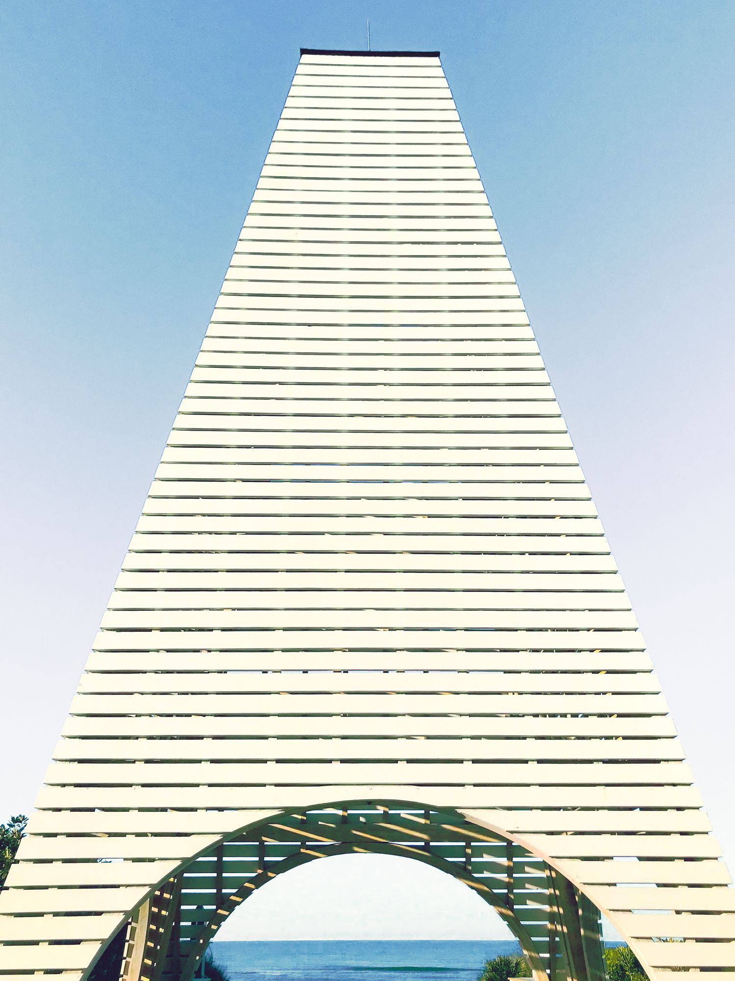 Modern white architectural structure with horizontal lines and an arched opening framing the ocean view.