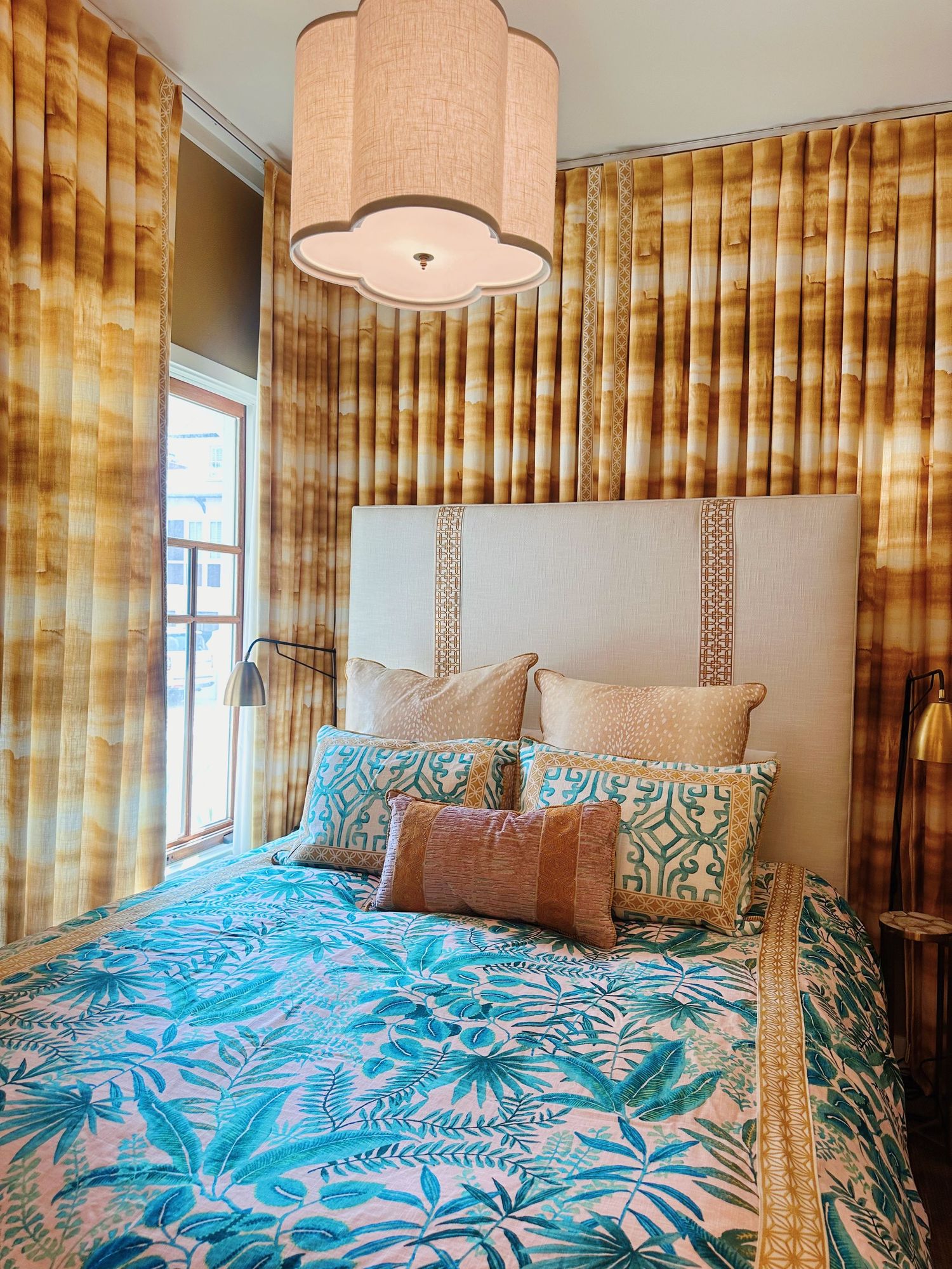 Modern bedroom featuring blue floral bedding, gold curtains, white headboard and large drum pendant light fixture.