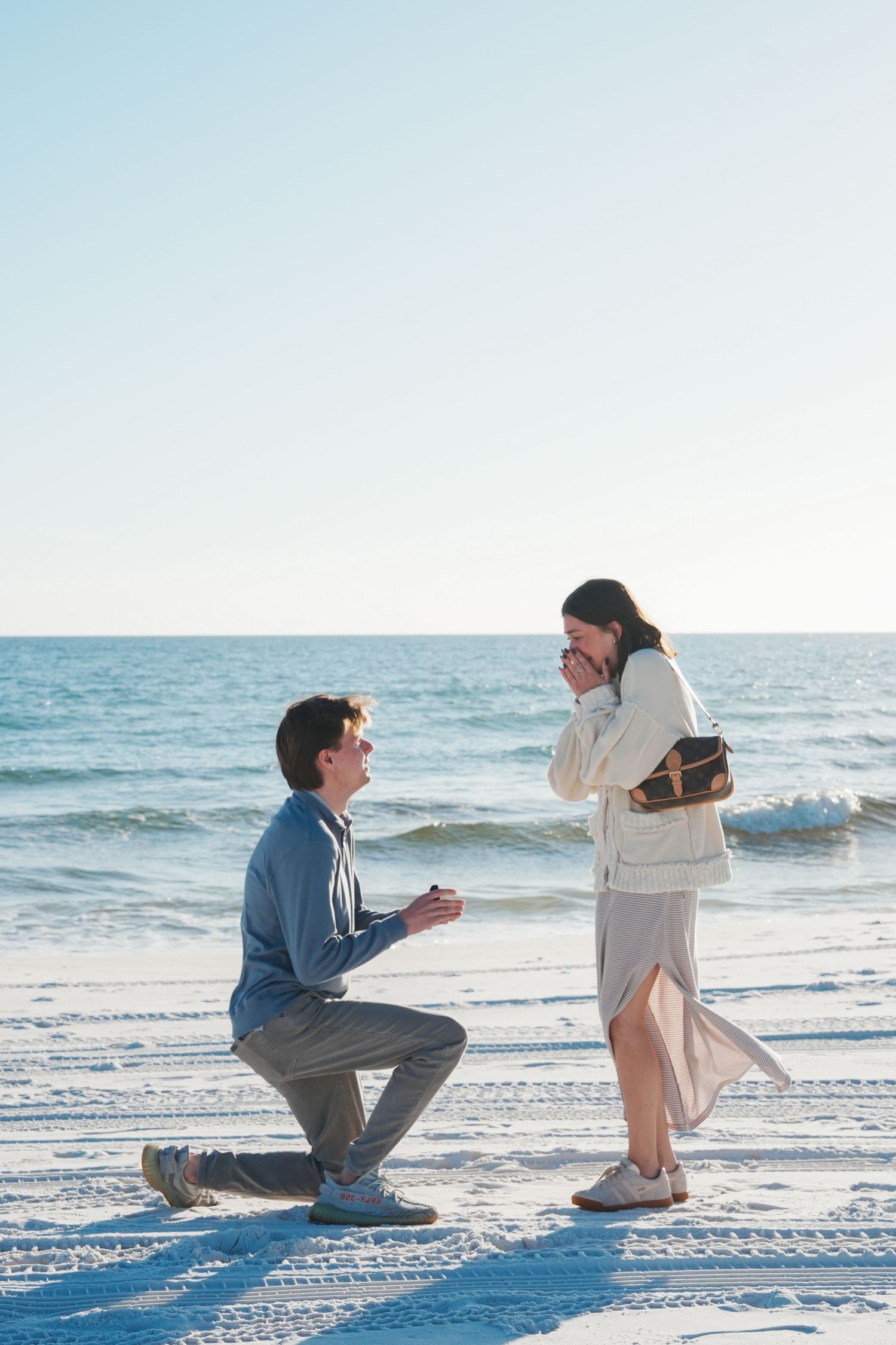 A romantic beach proposal sequence showing a couple in winter attire during a sunset marriage proposal on white sand.
