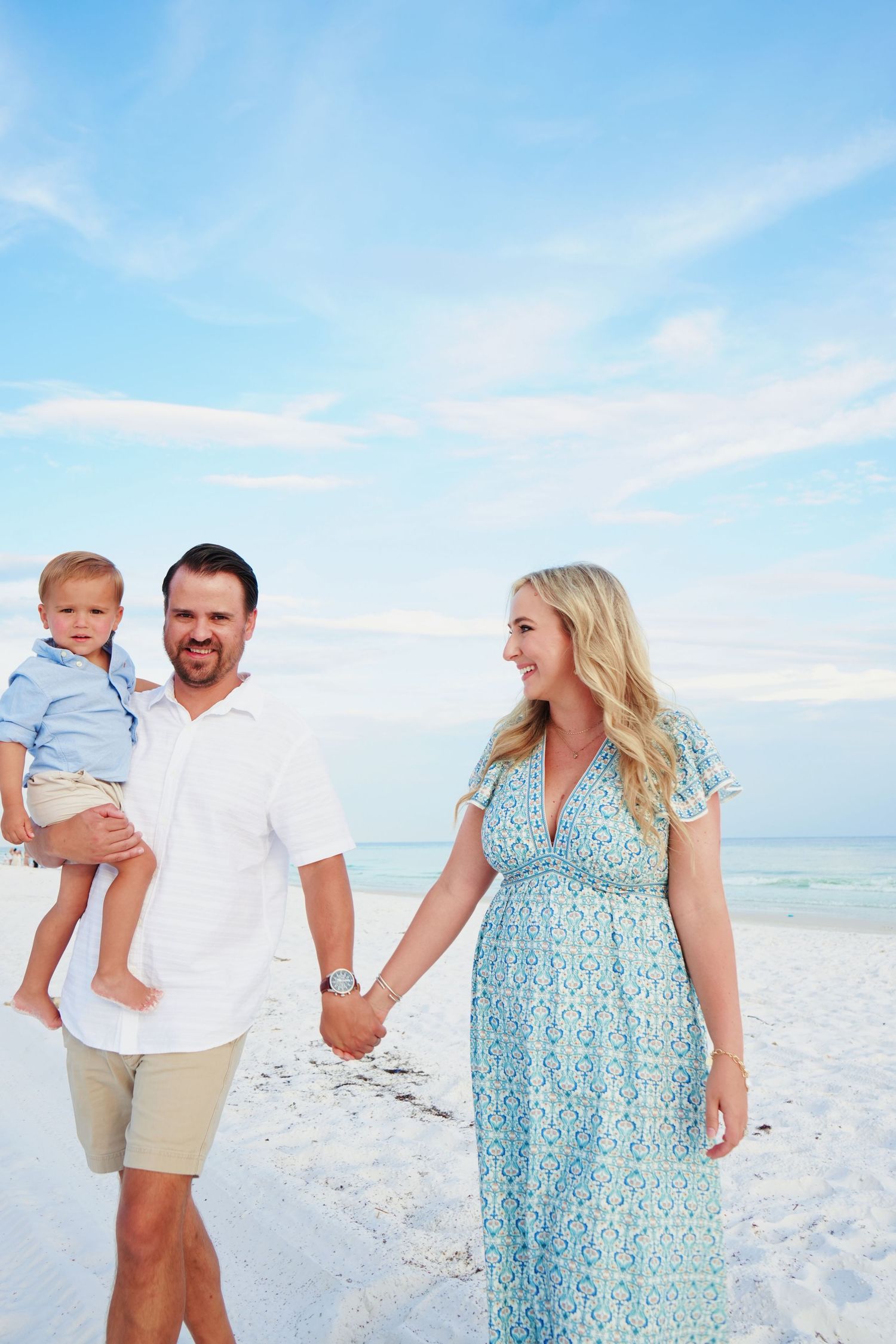 Family wearing white and blue outfits poses together on pristine white sand beach.