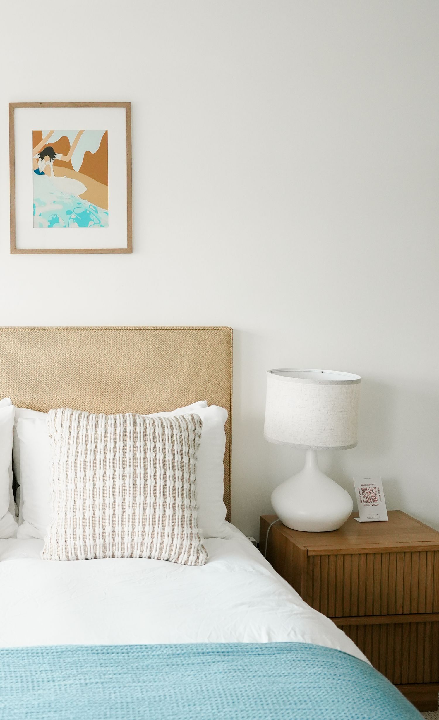 Two twin beds with white linens and turquoise throws are positioned side by side against a neutral wall with framed artwork.