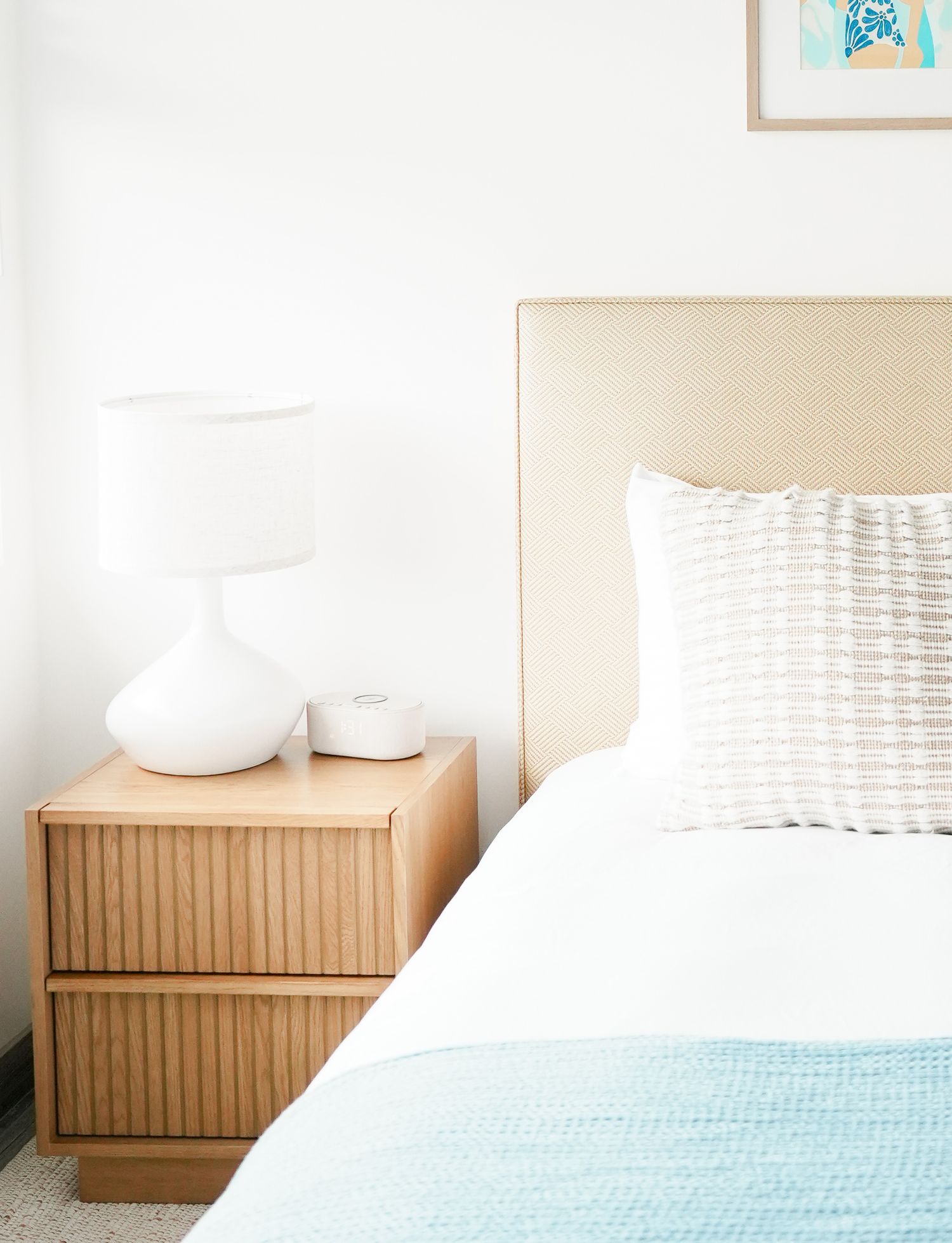 A modern bedroom featuring a bed with light blue bedding and wooden nightstands in a bright, minimalist setting.