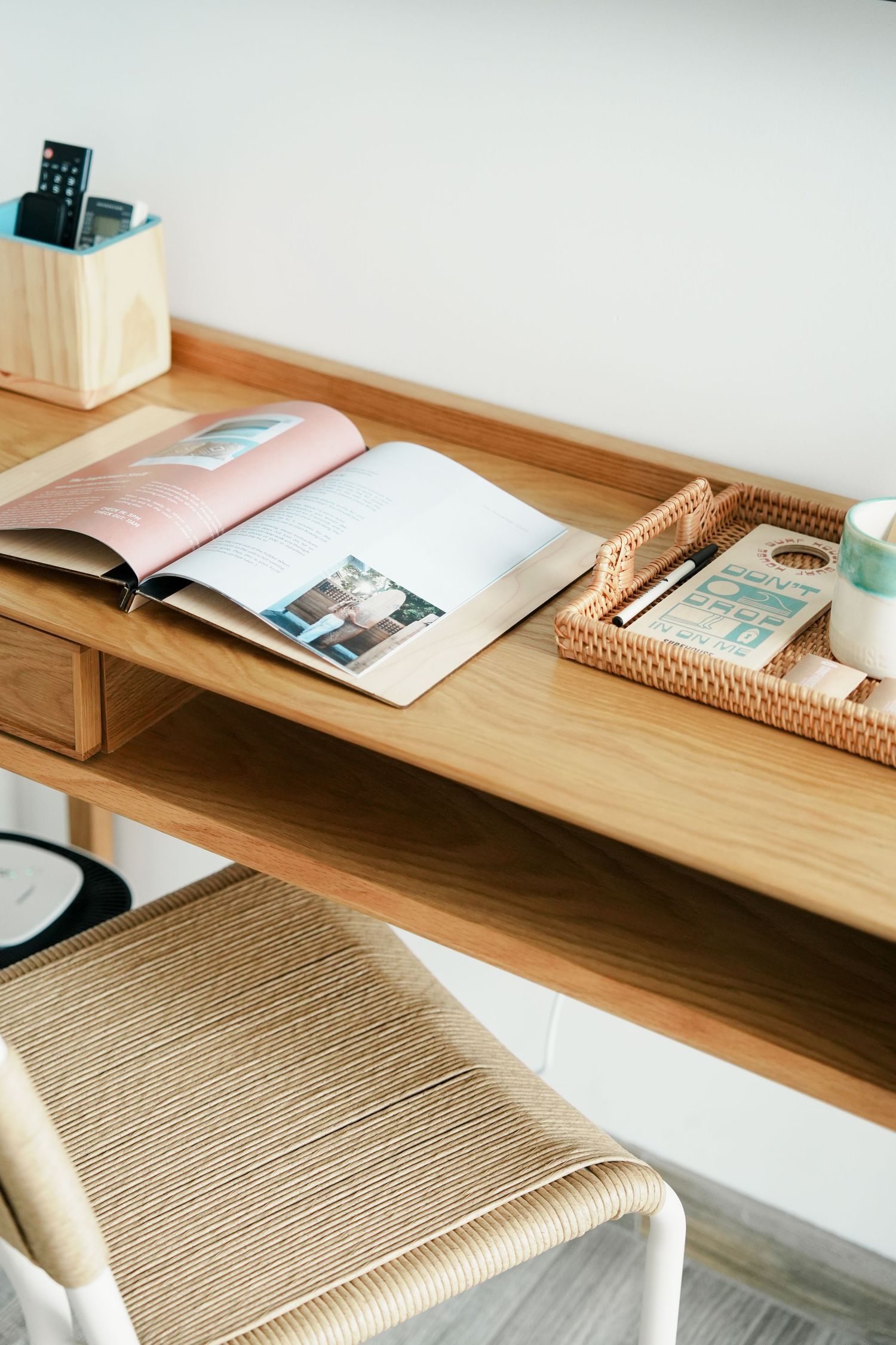 Minimalist wooden desk setup with woven chair and organized workspace accessories.