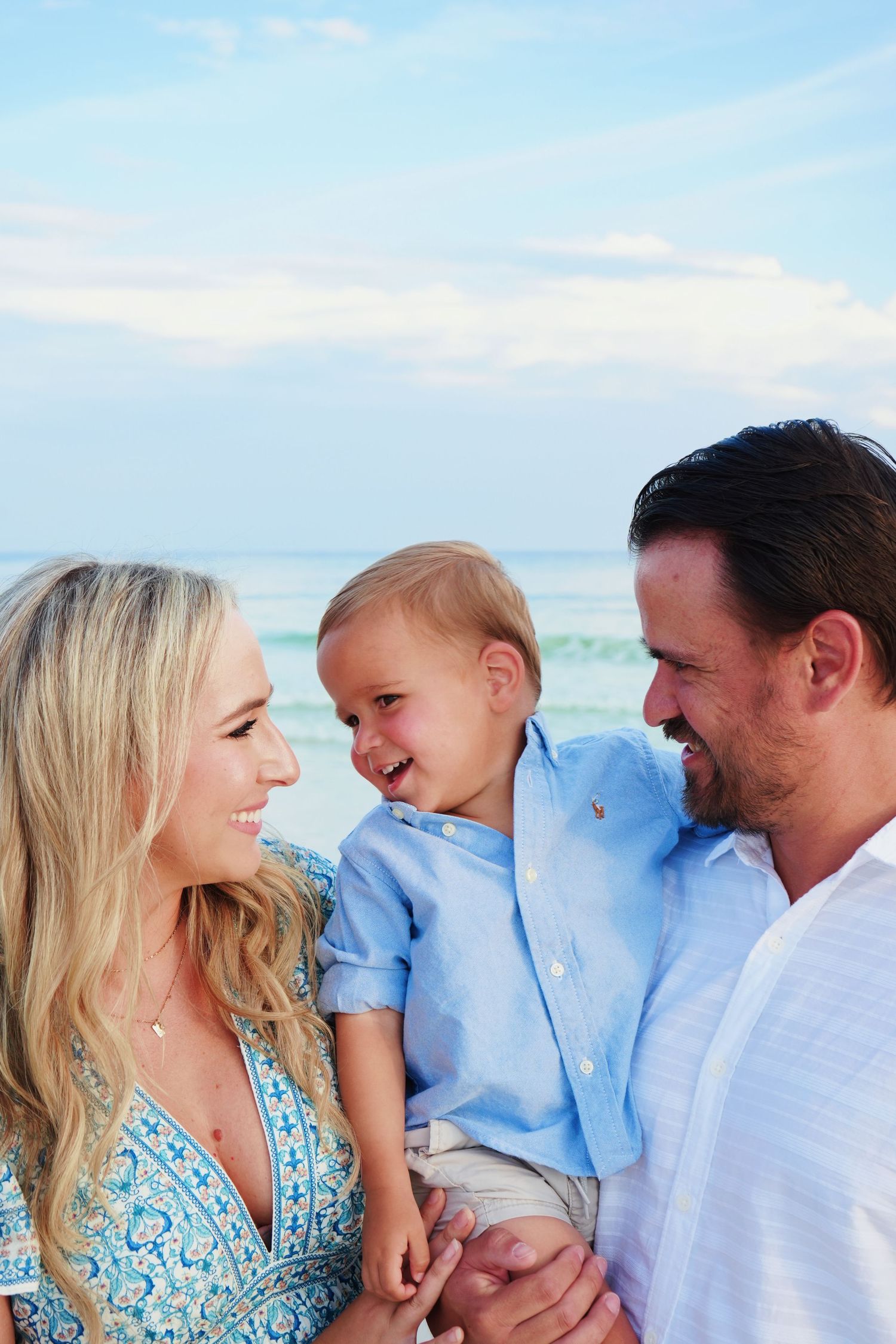 A happy moment between a couple and child laughing together at the beach against a bright blue sky in summer.