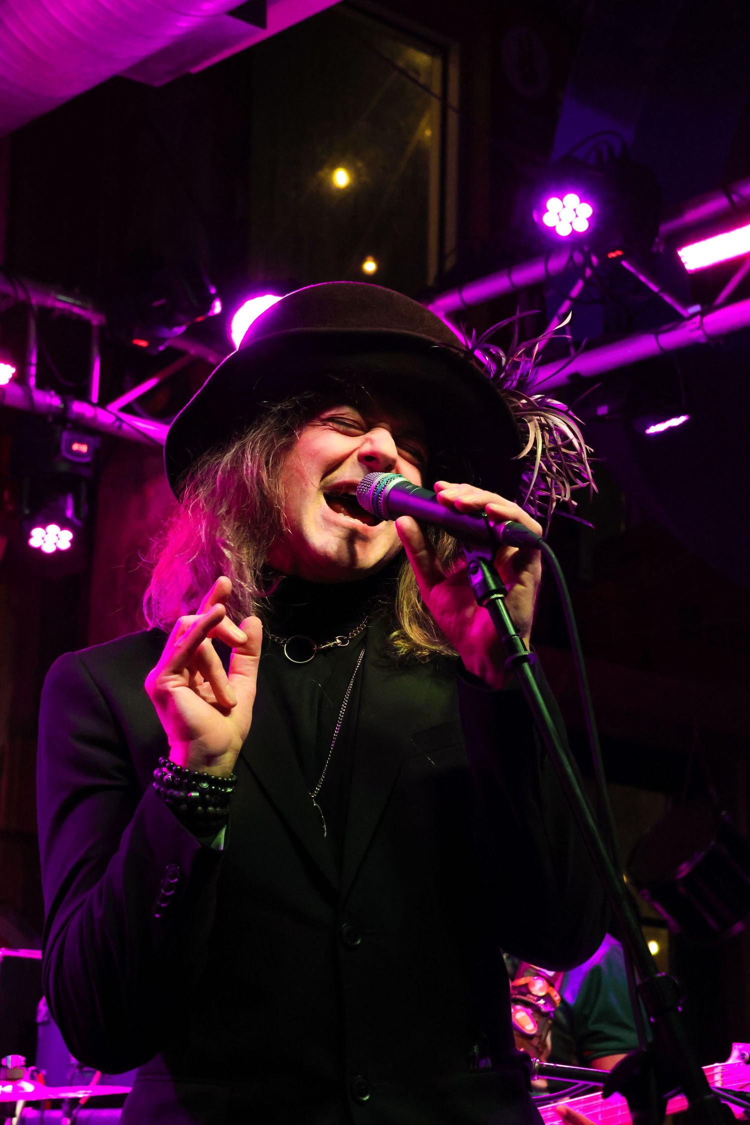 Singer performing on stage with dramatic purple lighting and wearing black hat.