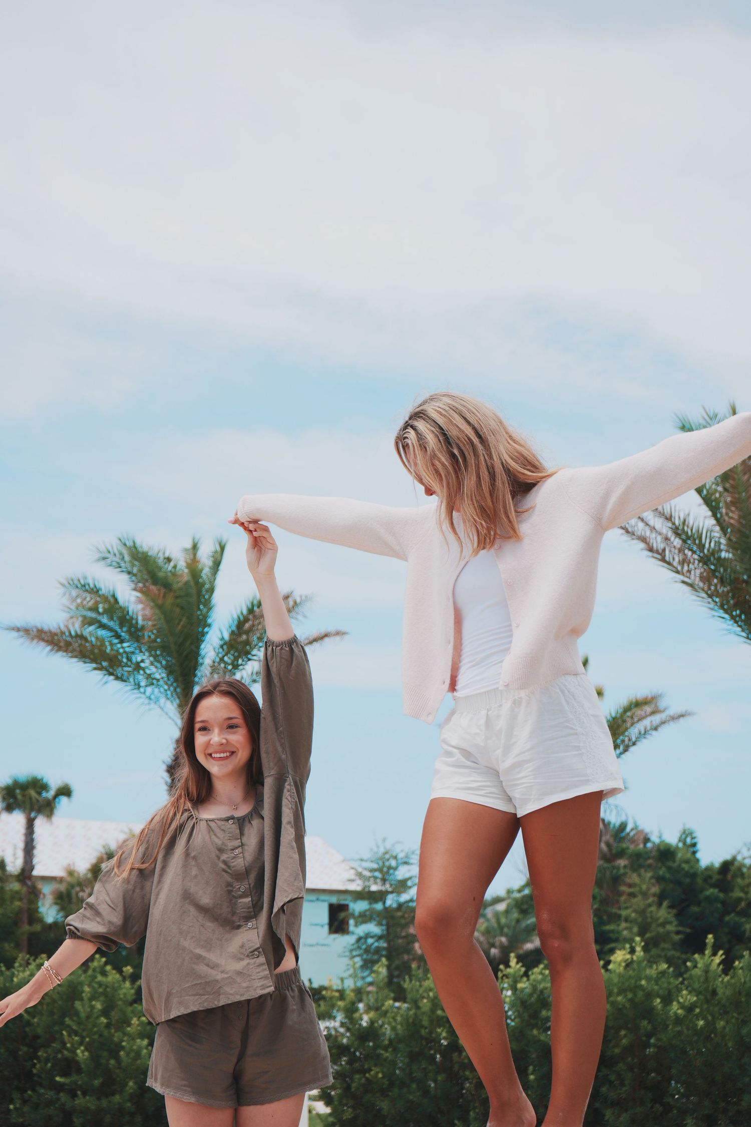 Two friends enjoying a carefree moment outdoors with palm trees and blue sky in the background.