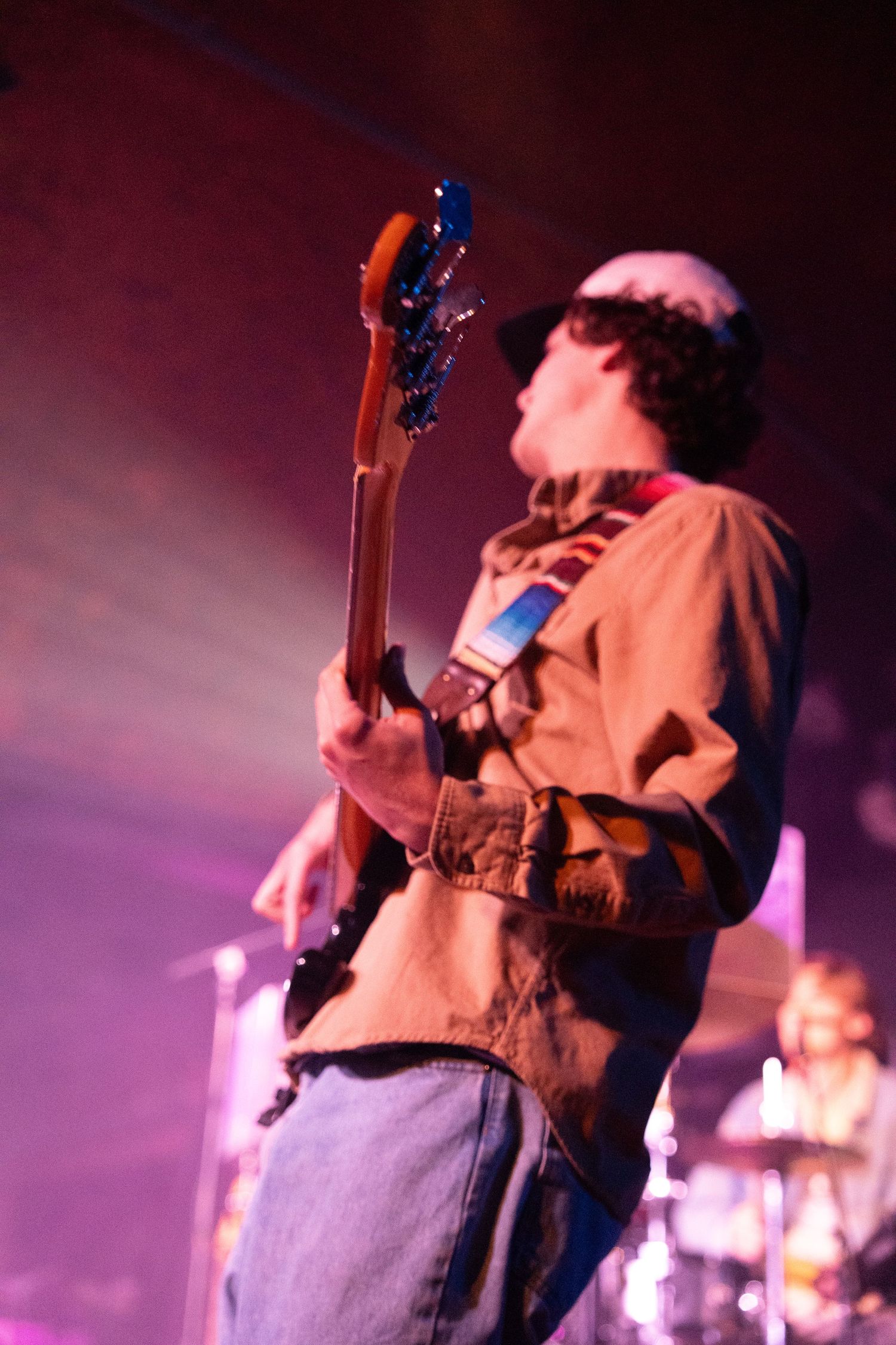 A musician performs on stage with a guitar under dramatic purple stage lighting.