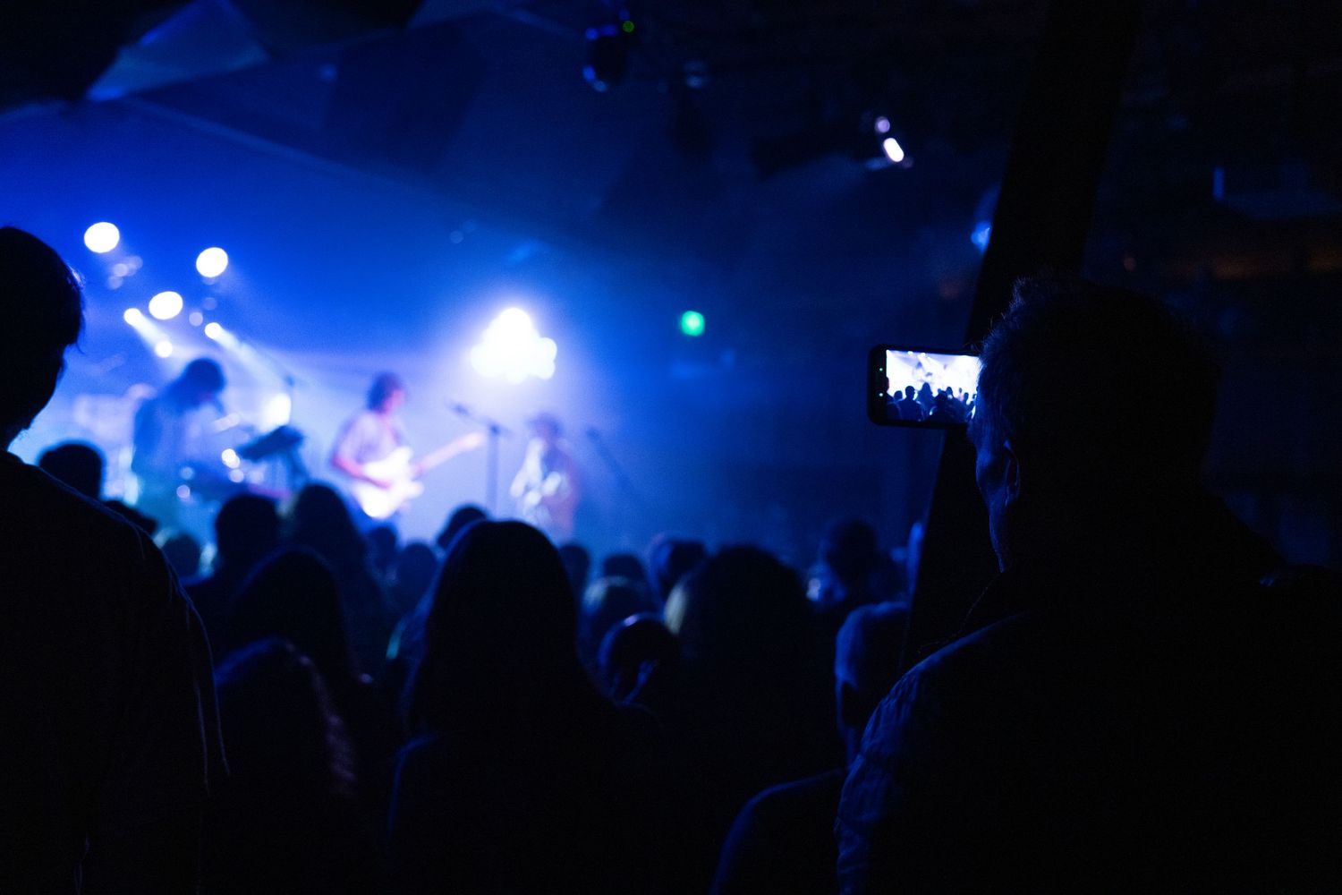 Silhouettes of concert crowd against bright blue stage lighting during a live music performance.