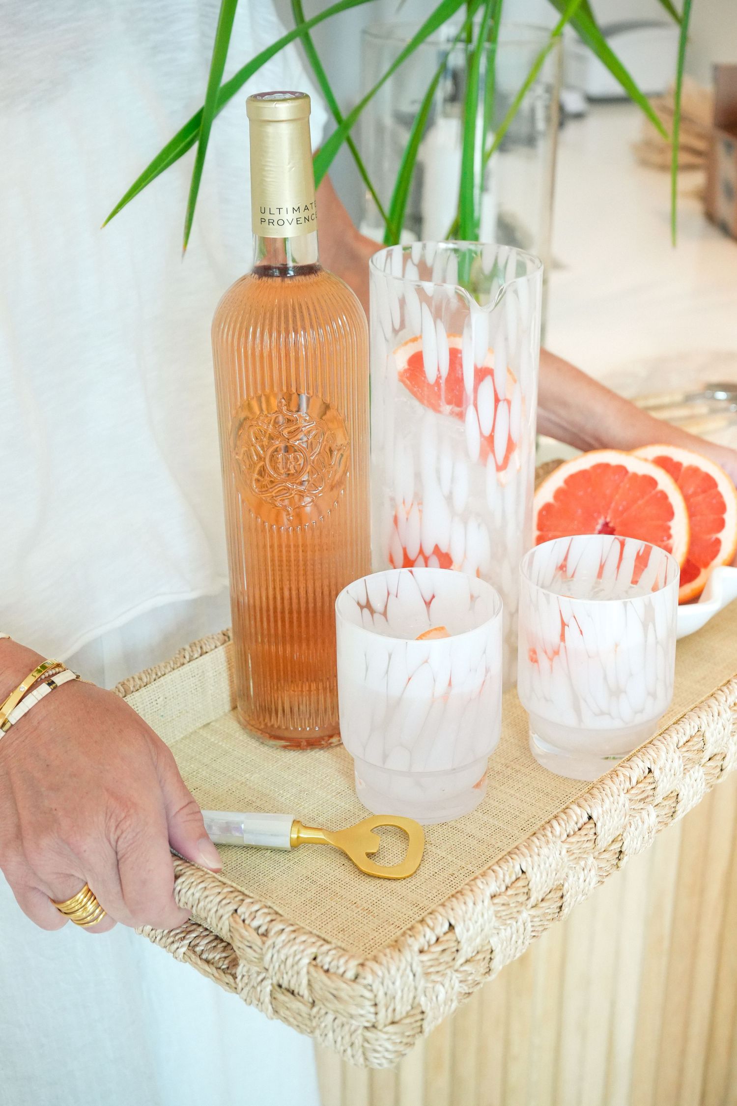 Elegant rose wine bottle and marbled glasses arranged on a fringed tray with fresh citrus and tropical decor.