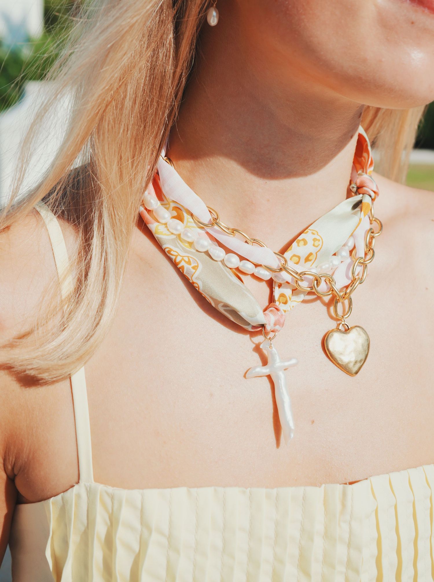 Close-up view of a delicate gold heart pendant necklace on a light yellow fabric background.