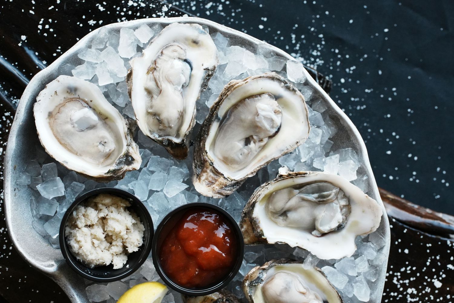 Fresh raw oysters on ice served with cocktail sauce and lemon wedges on a silver platter.
