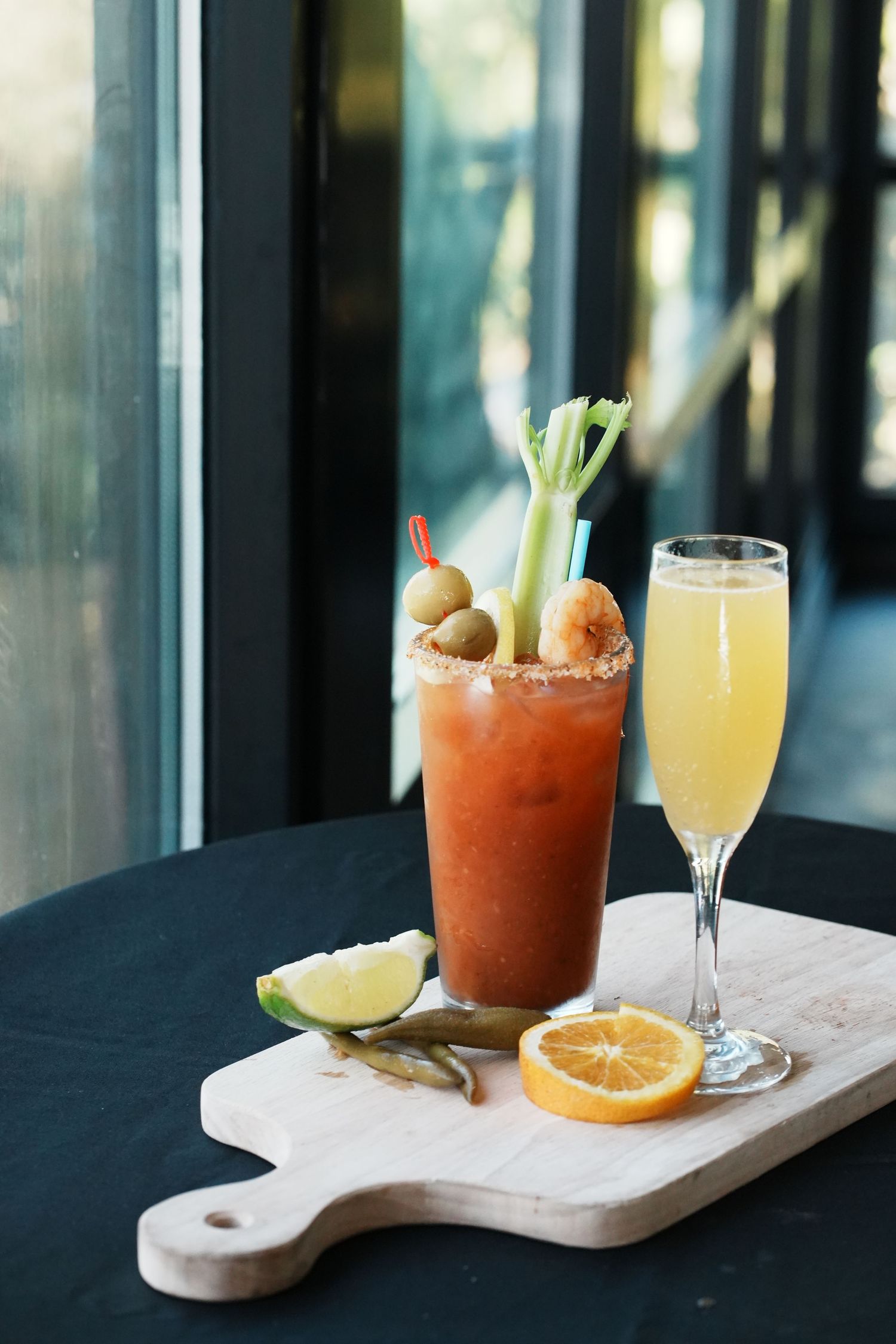 Bloody Mary cocktail and mimosa served on wooden board with citrus garnish.