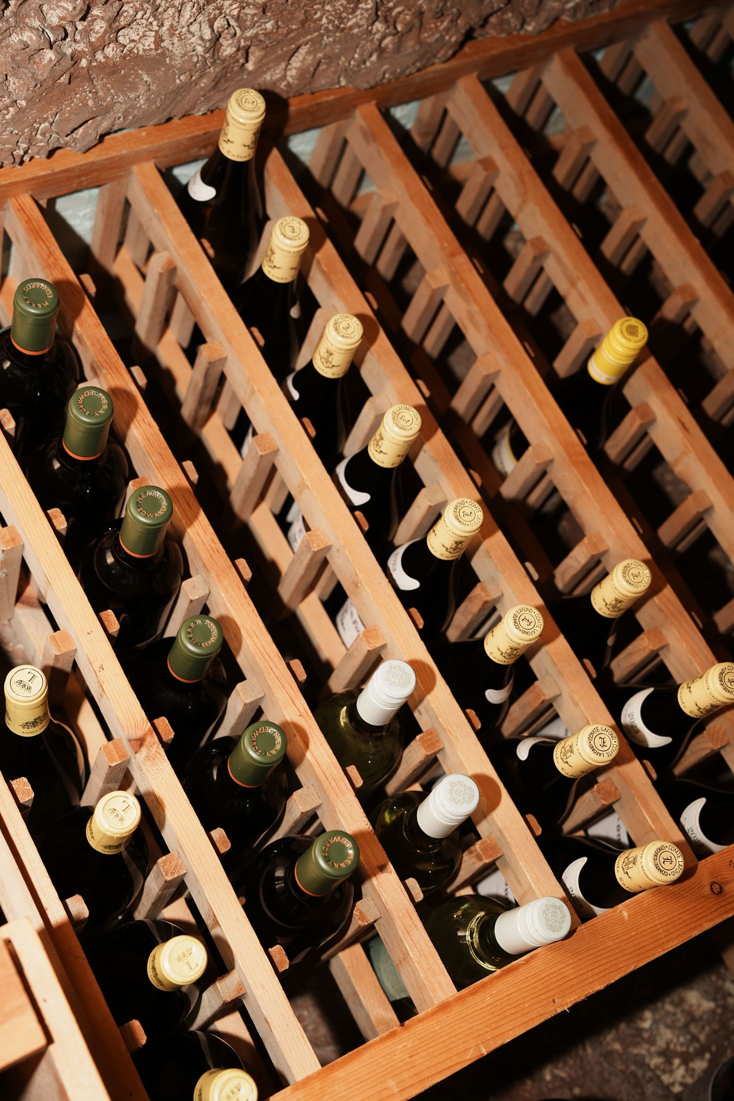 Rows of wine bottles stored diagonally in a wooden wine rack with visible corks and labels.