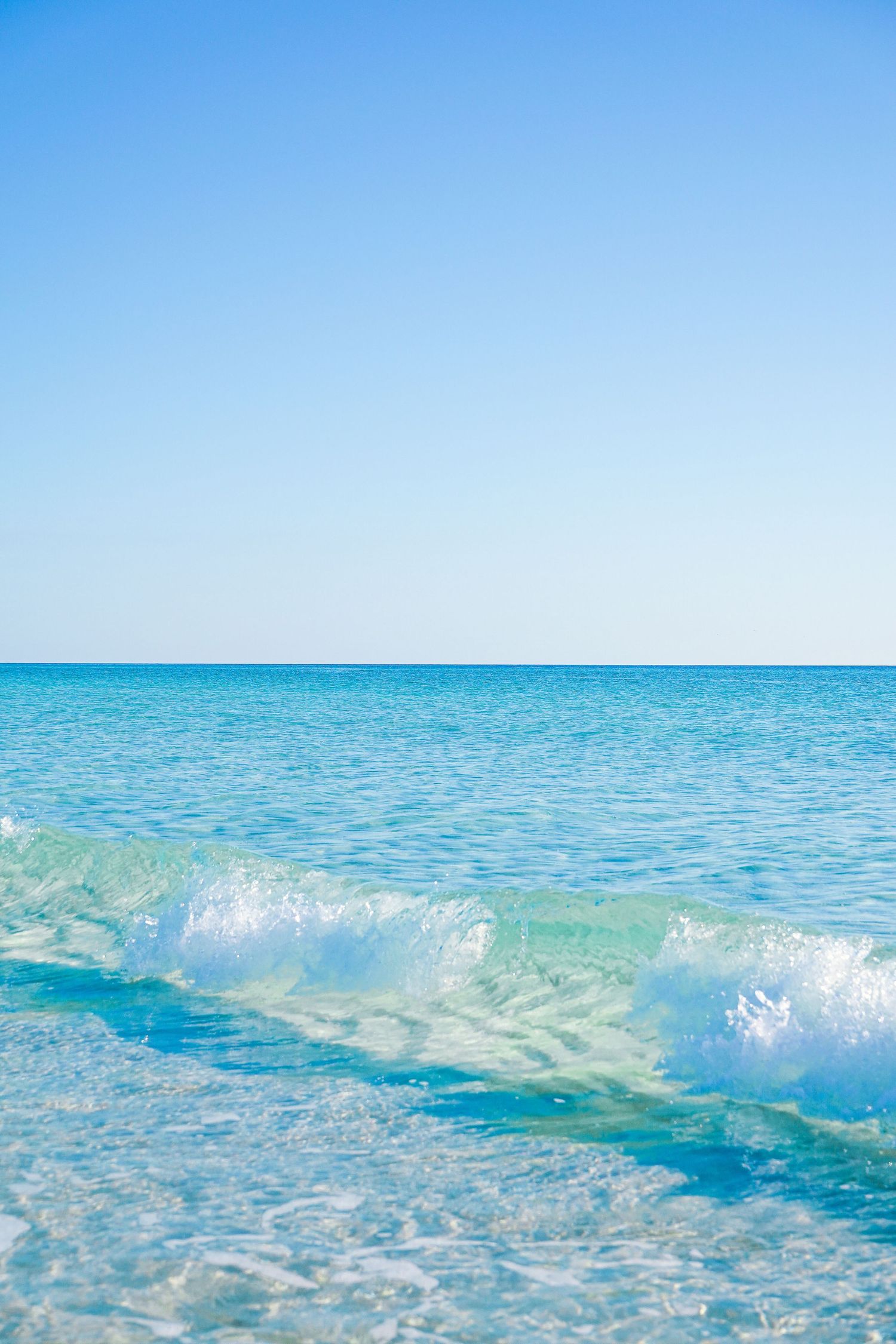 Breaking turquoise waves rolling onto shore under clear blue skies.