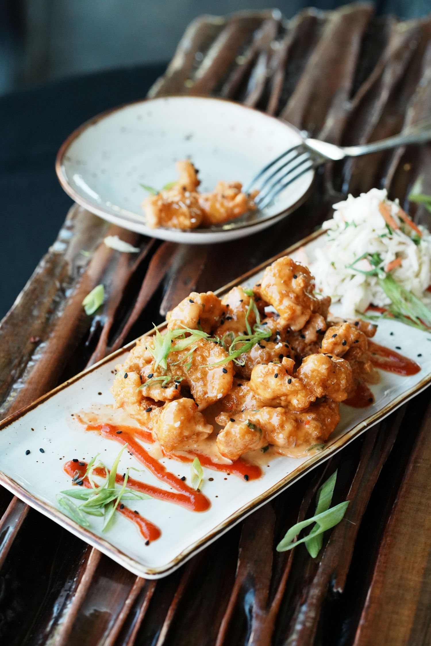 Crispy fried cauliflower bites plated with sauce and garnishes on a white rectangular plate.