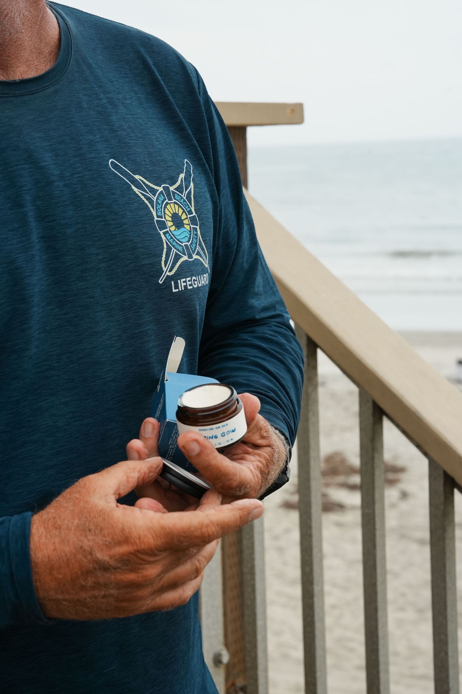 Close-up series showing hands holding a coffee cup against a beachside railing with a hummingbird logo on a navy shirt.